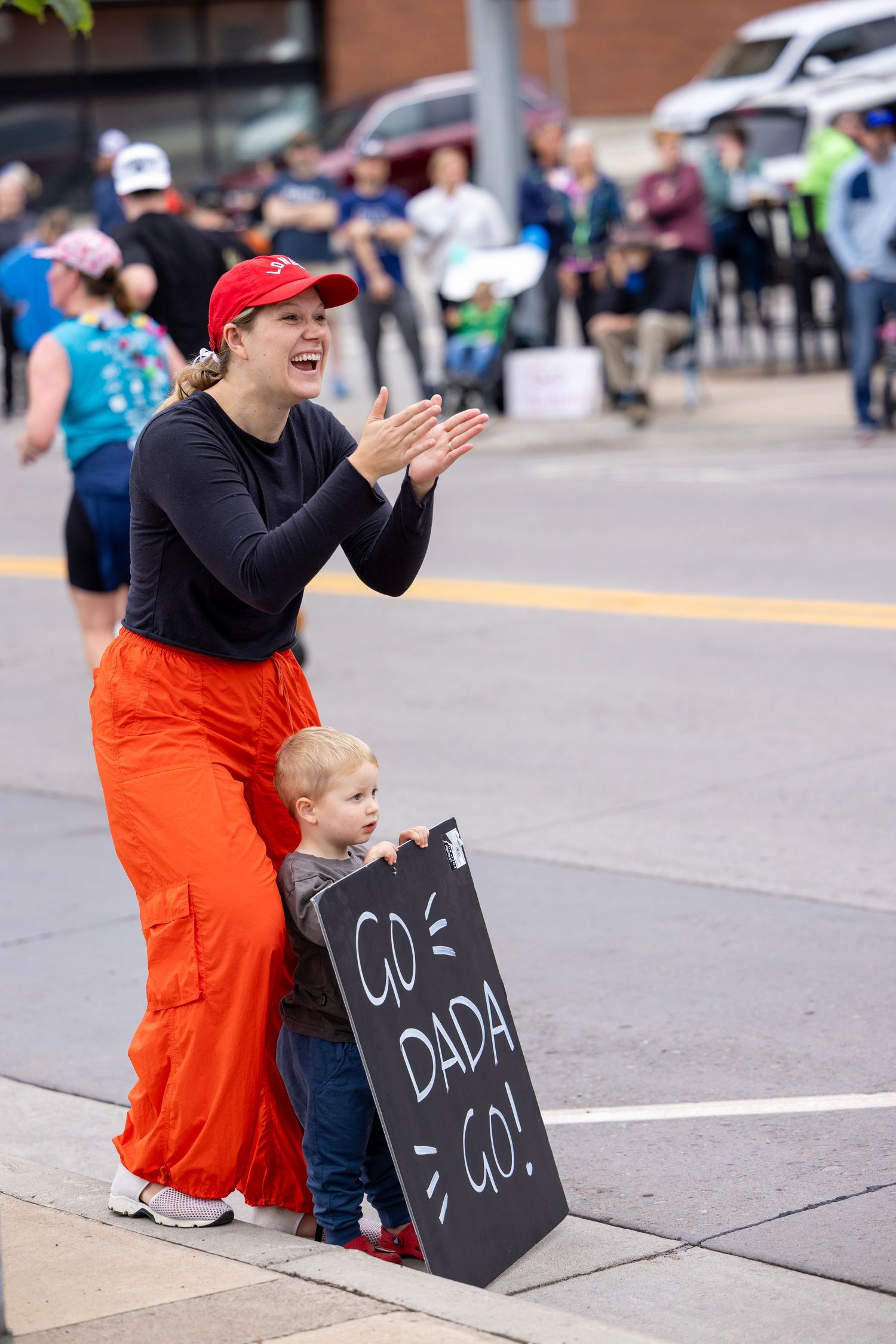 Spectators holding chalkboard signs cheer from the sidelines of a race.