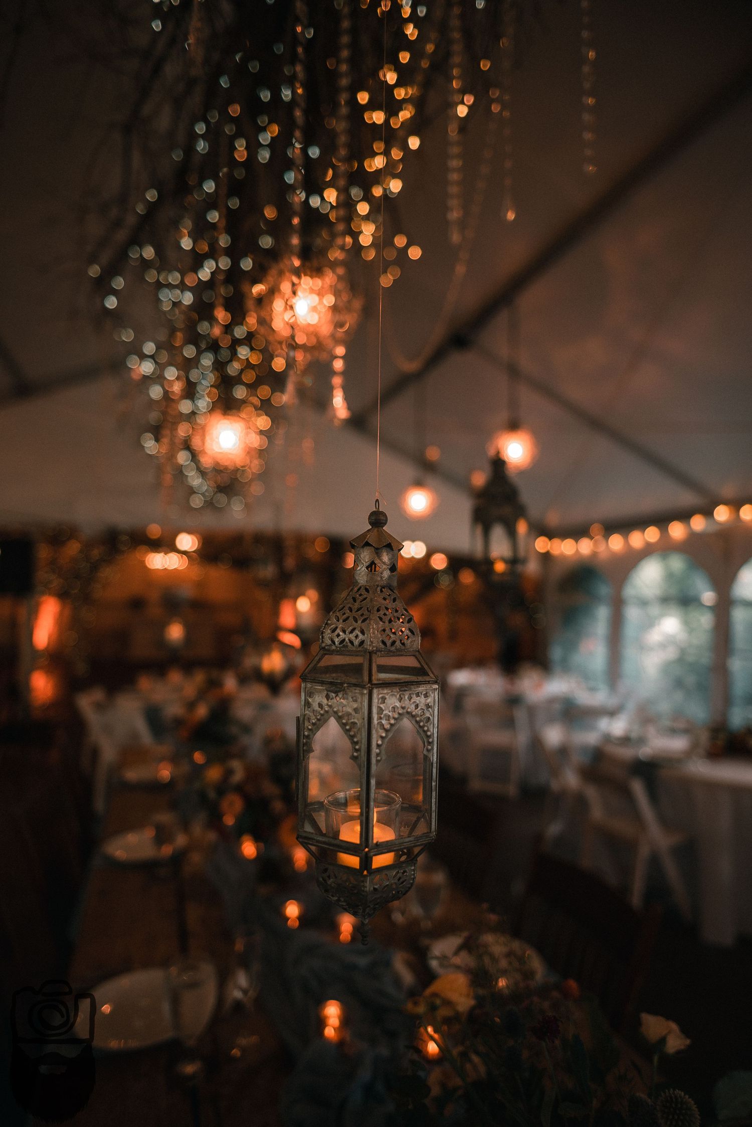 Vintage lanterns and string lights create romantic ambiance in a dimly lit wedding reception tent.