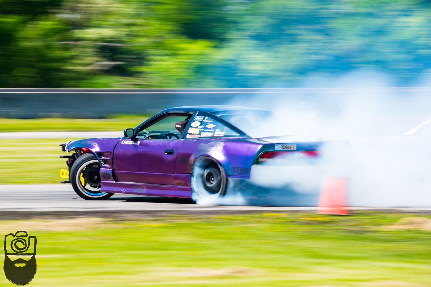 Purple drift car creating smoke while sliding through a corner on a racetrack.