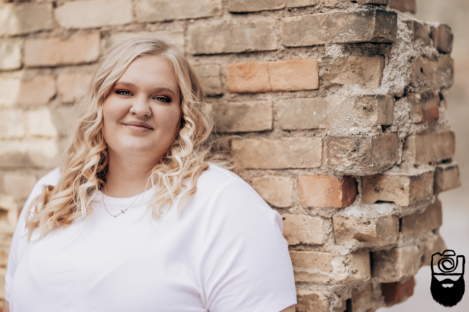 Portrait against rustic brick wall wearing white top.