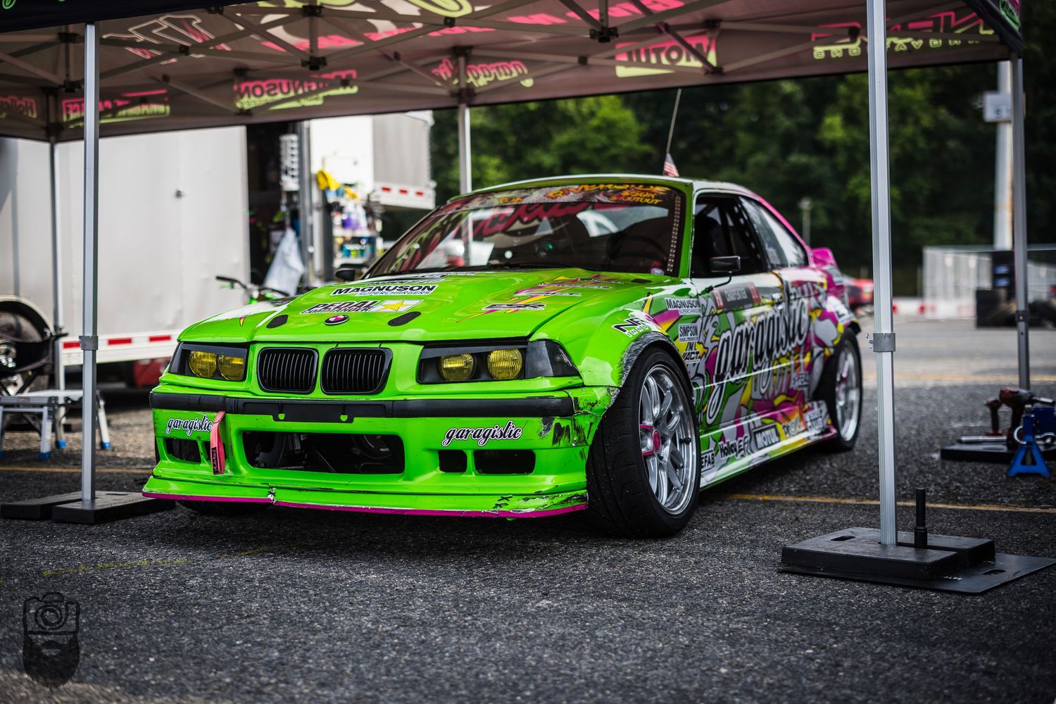 Bright green custom drift car with racing livery parked under covered area.