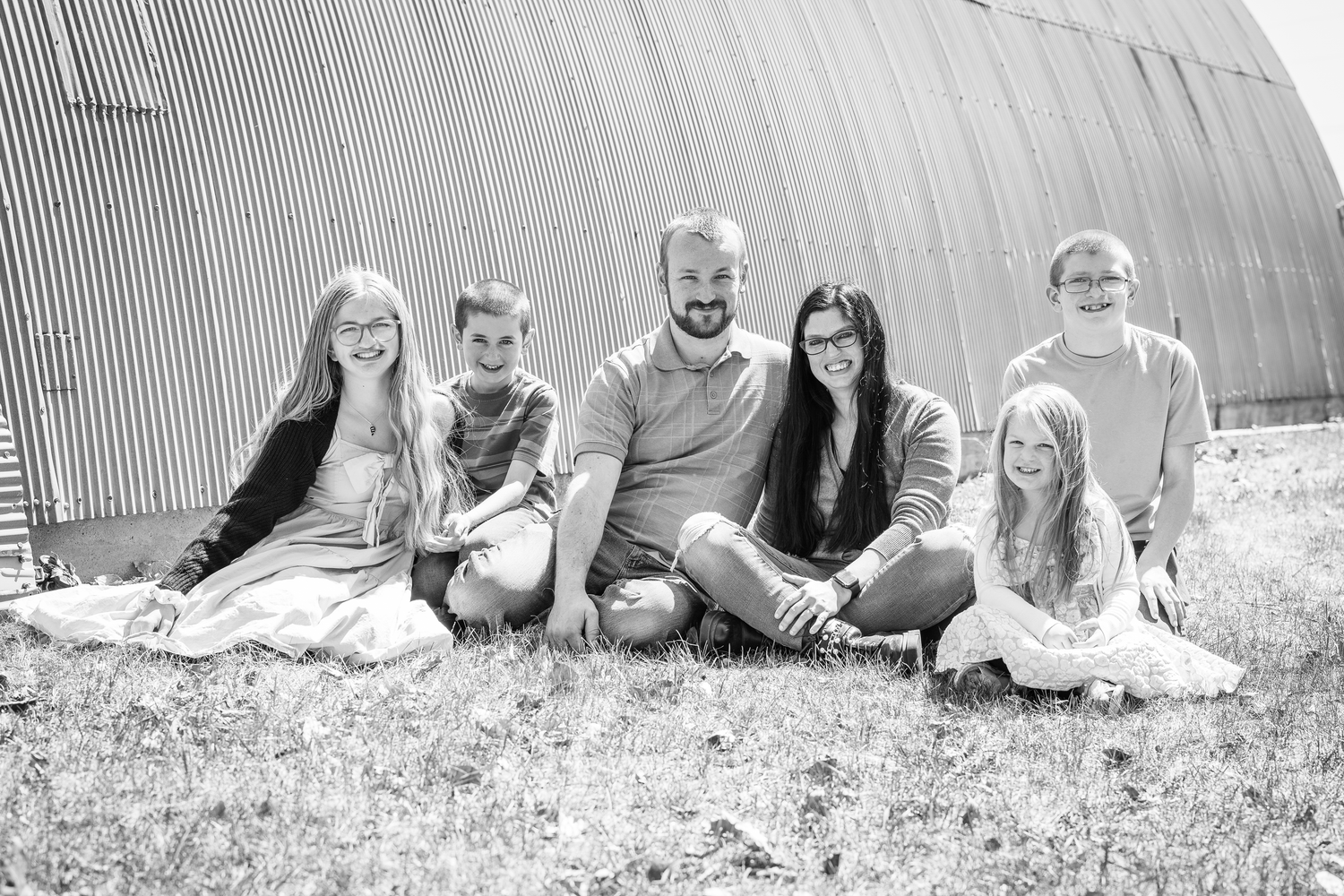 A family group sits casually against a curved metal building wall in black and white.