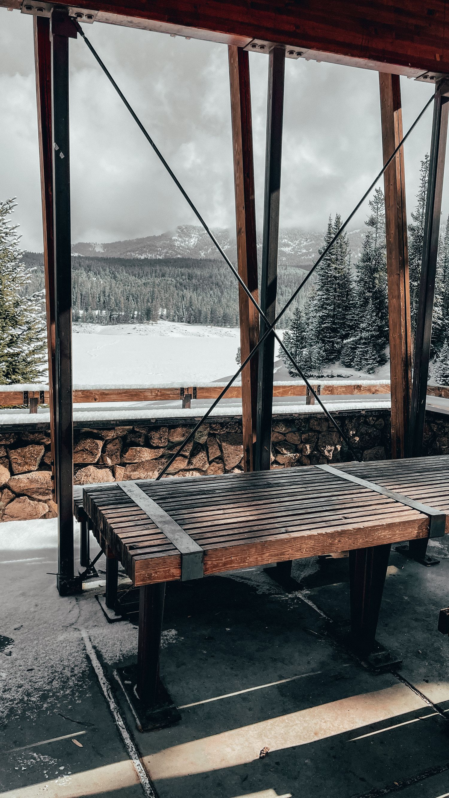 Rustic wooden bench overlooking snowy mountain landscape from covered viewing area.