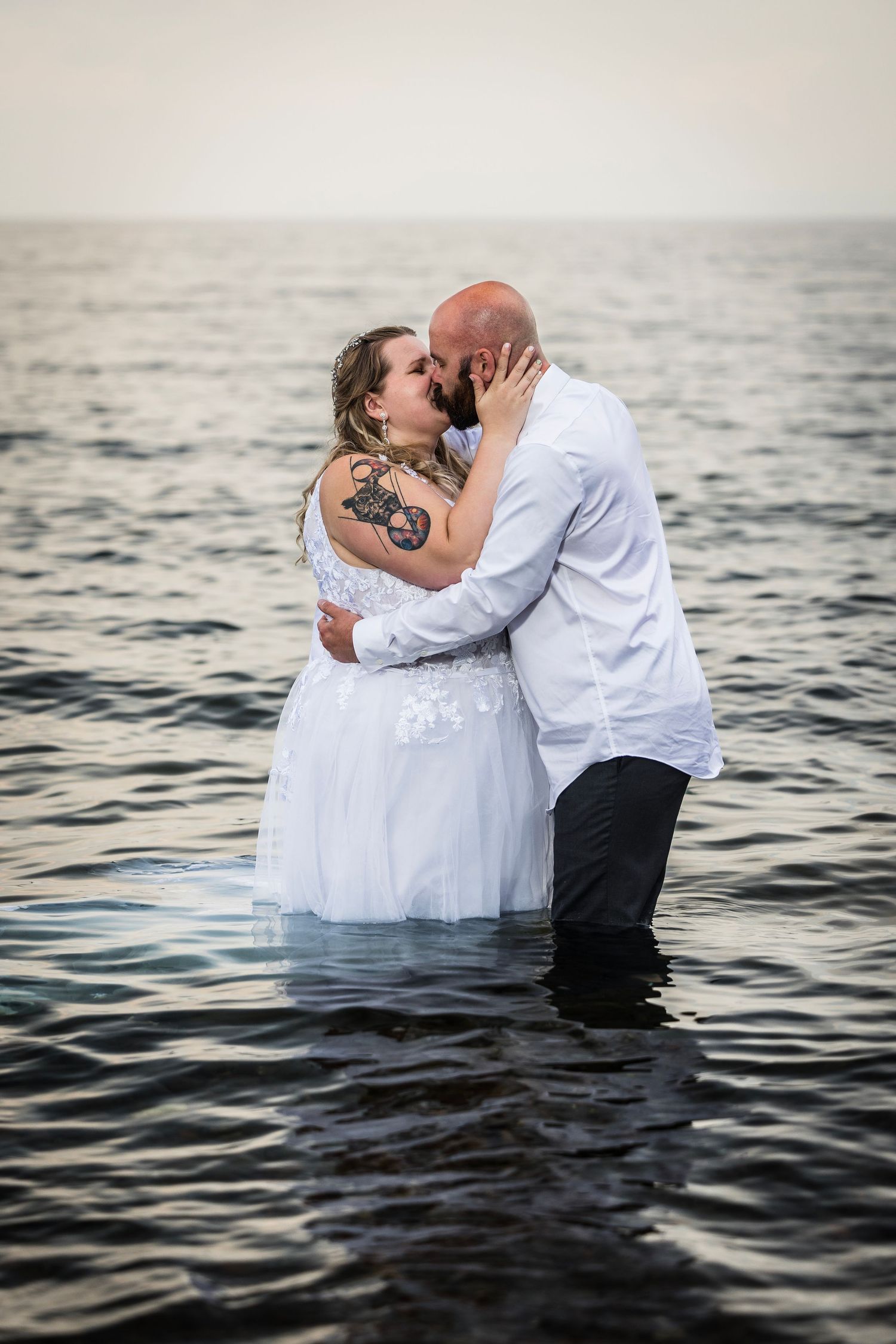 A romantic wedding photoshoot in the ocean at sunset with a couple embracing in the water.
