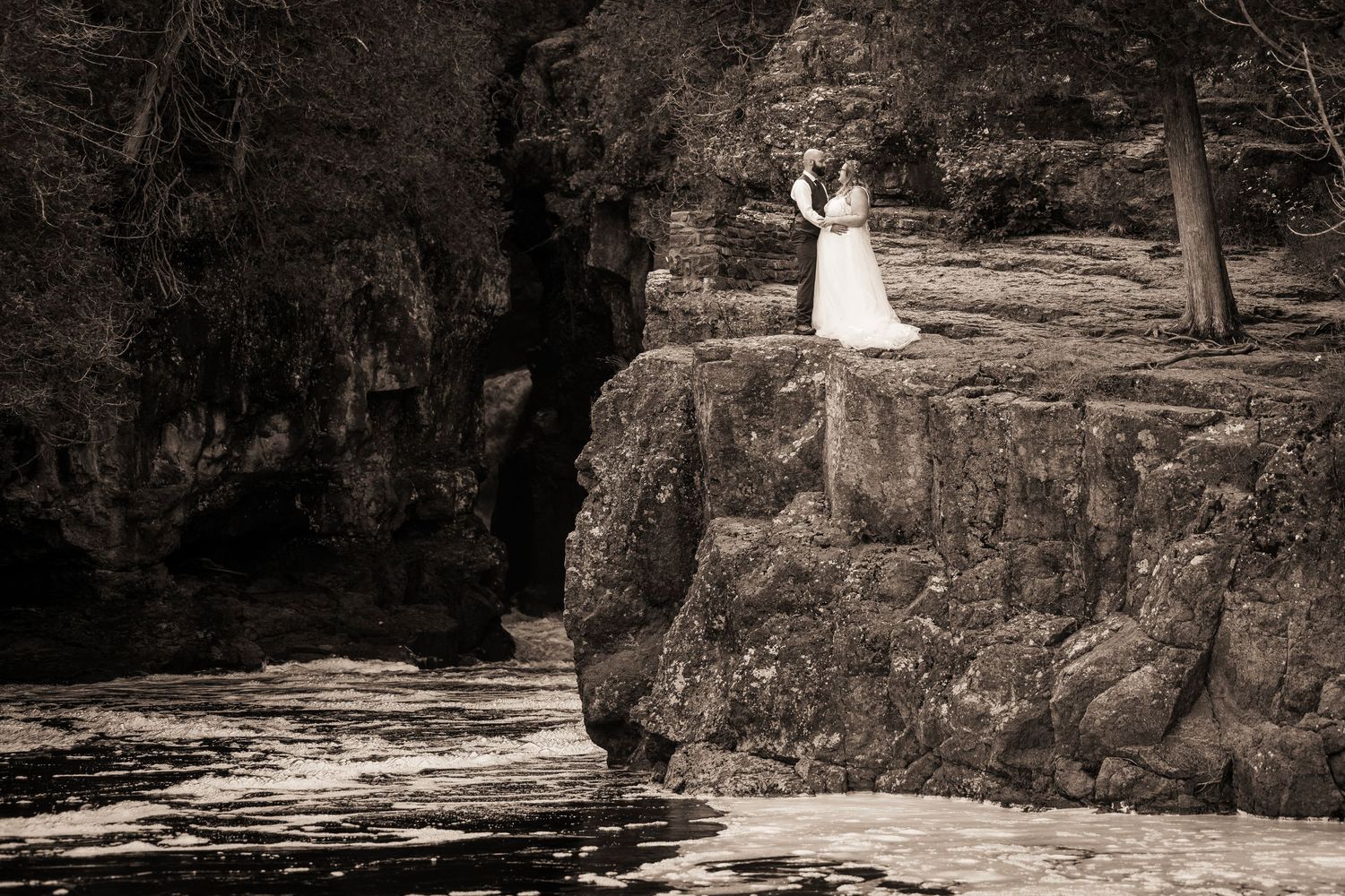 A sepia-toned wedding photo on dramatic rocky cliffs.
