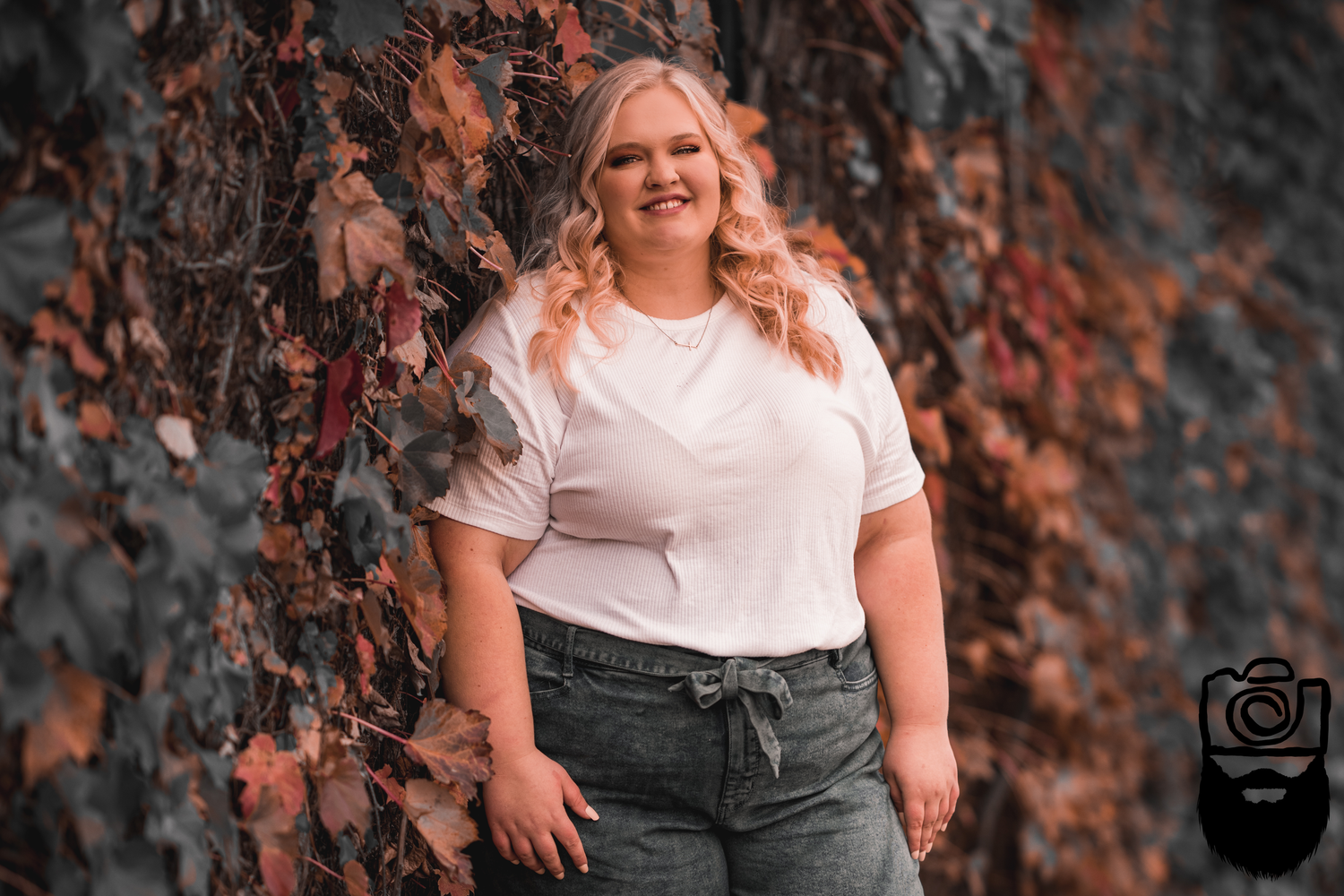 Portrait against autumn foliage backdrop wearing white t-shirt.