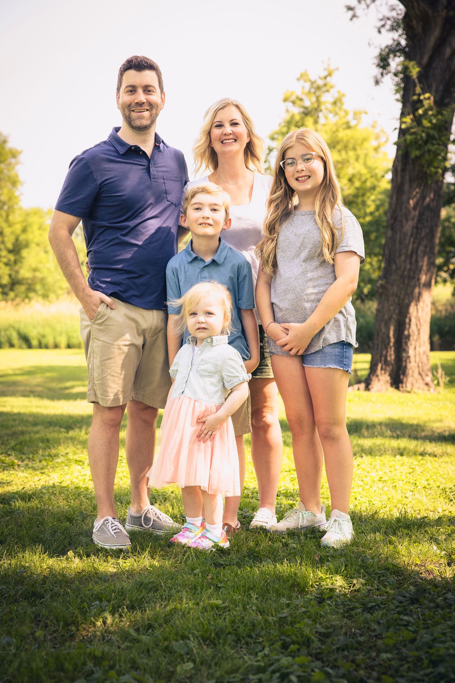 Family portrait series captured in warm evening sunlight on grassy hill.