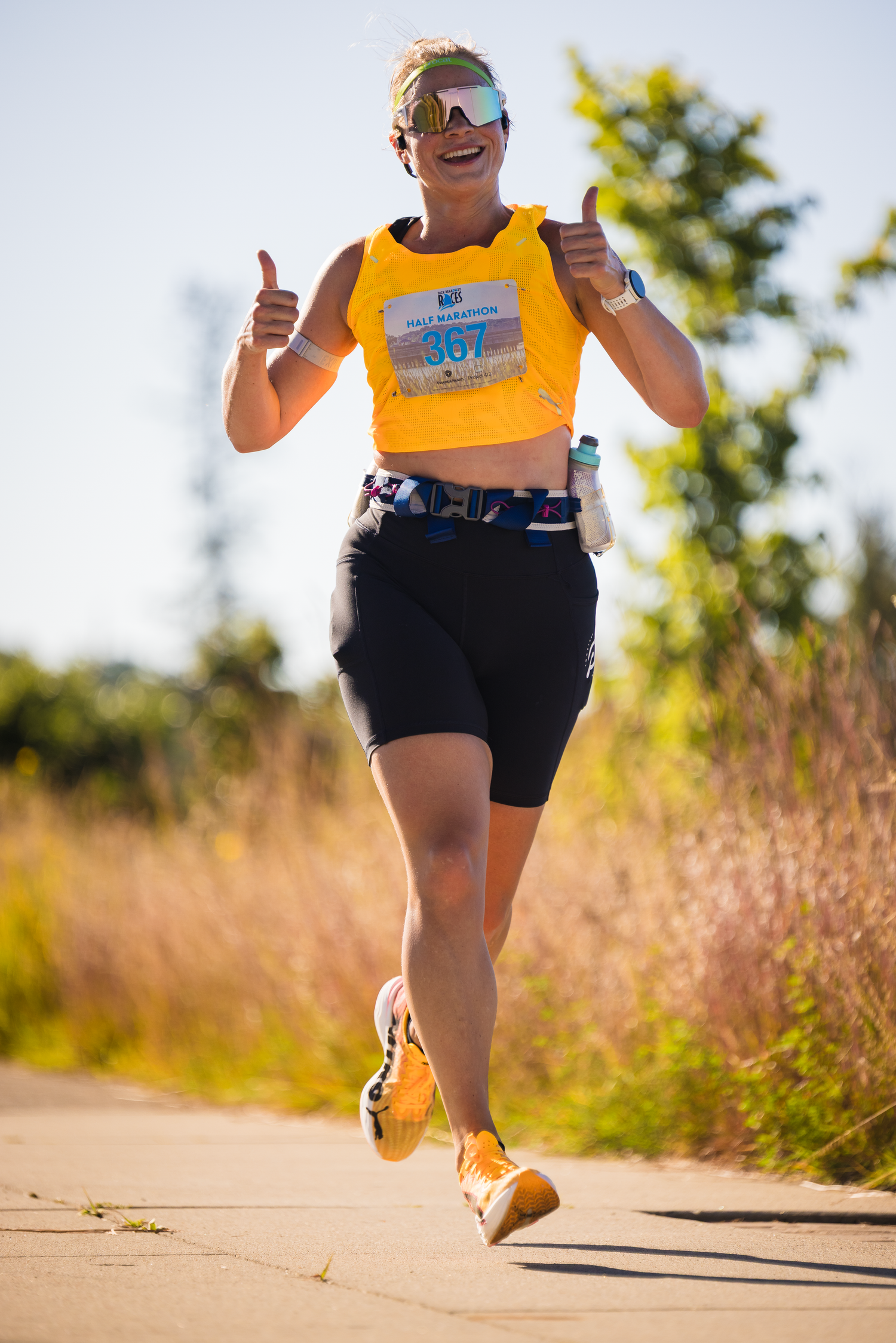 Runner wearing orange race bib and black shorts sprints along a dirt path during competition.
