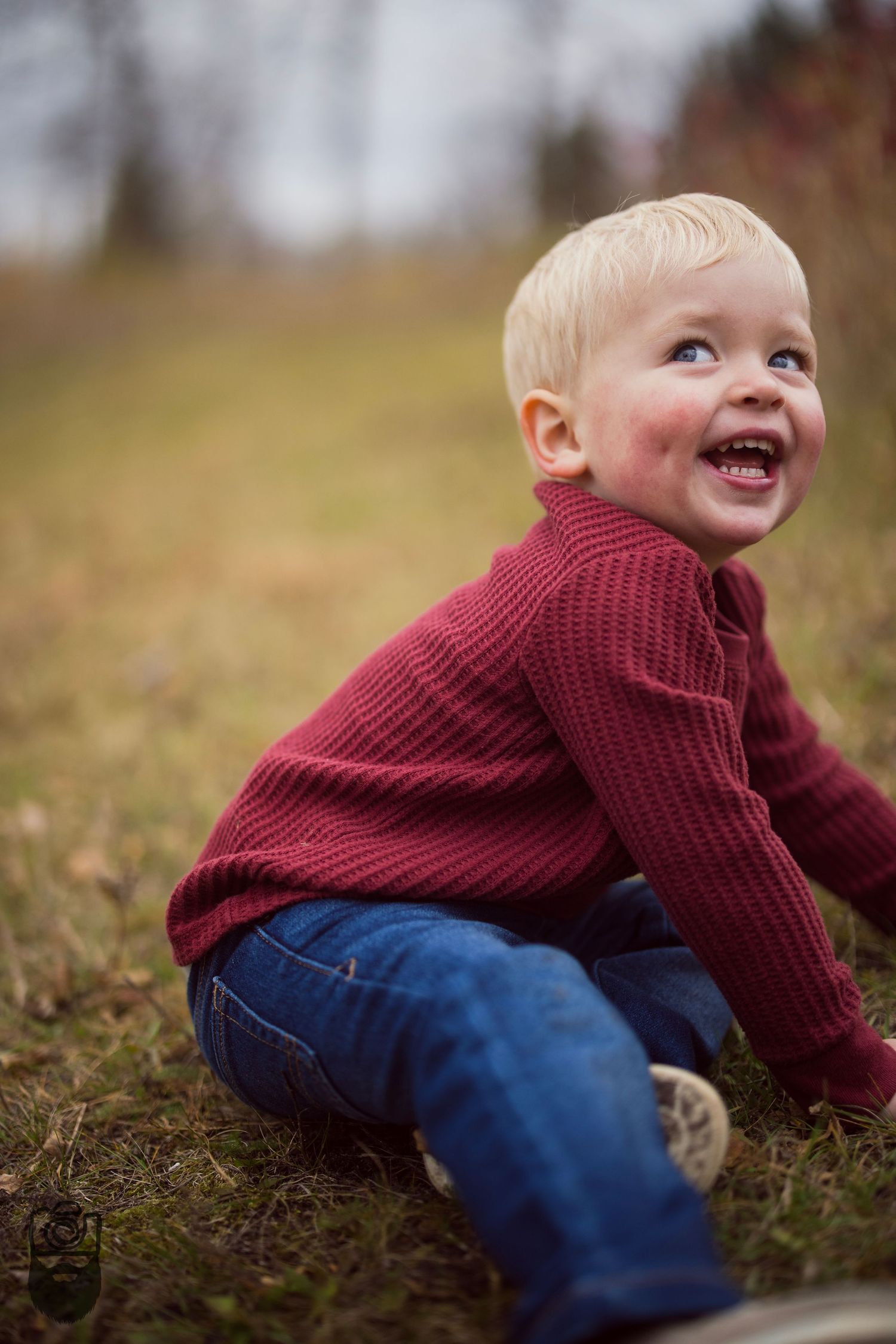 Young child in burgundy sweater crawling and laughing on autumn grass.