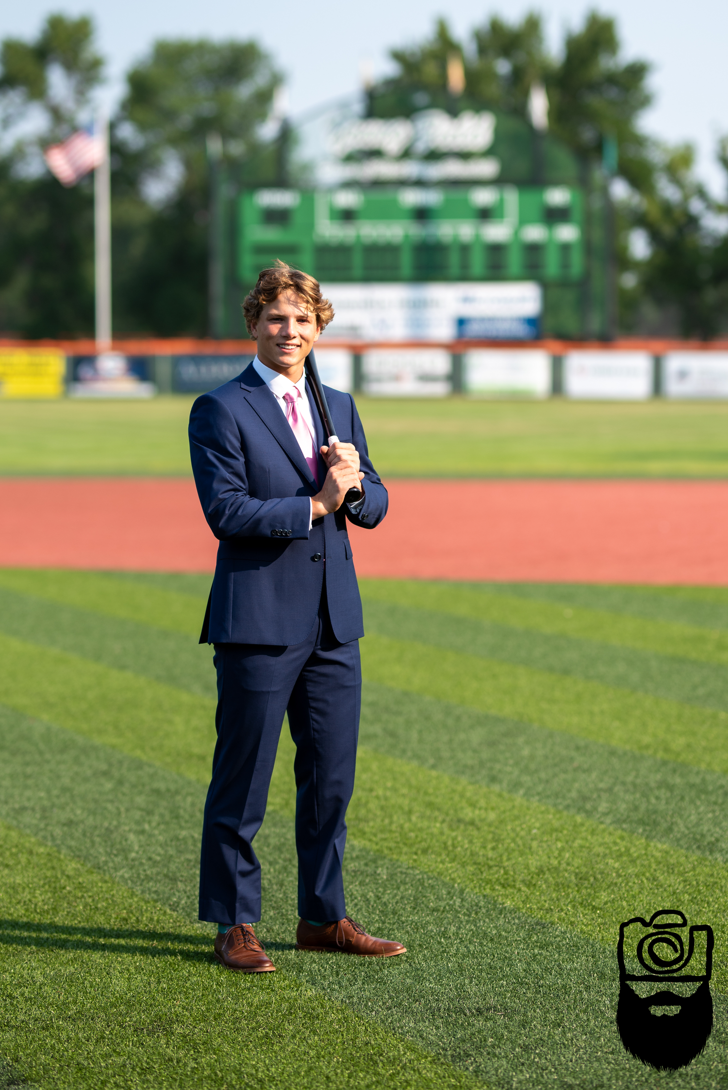 Person in navy suit standing on green sports field with stadium backdrop.