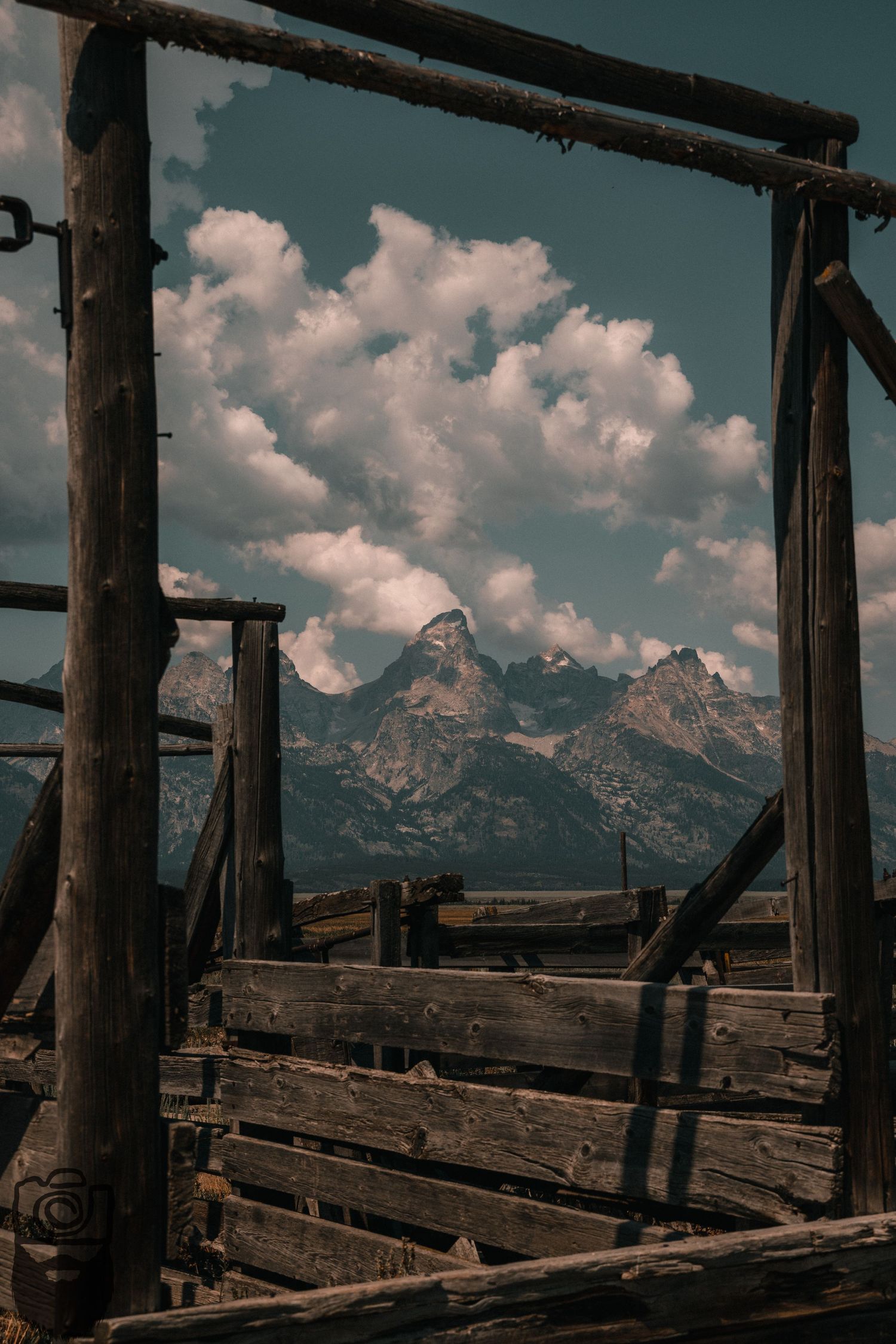 Rustic wooden beams frame a dramatic mountain range under puffy clouds.