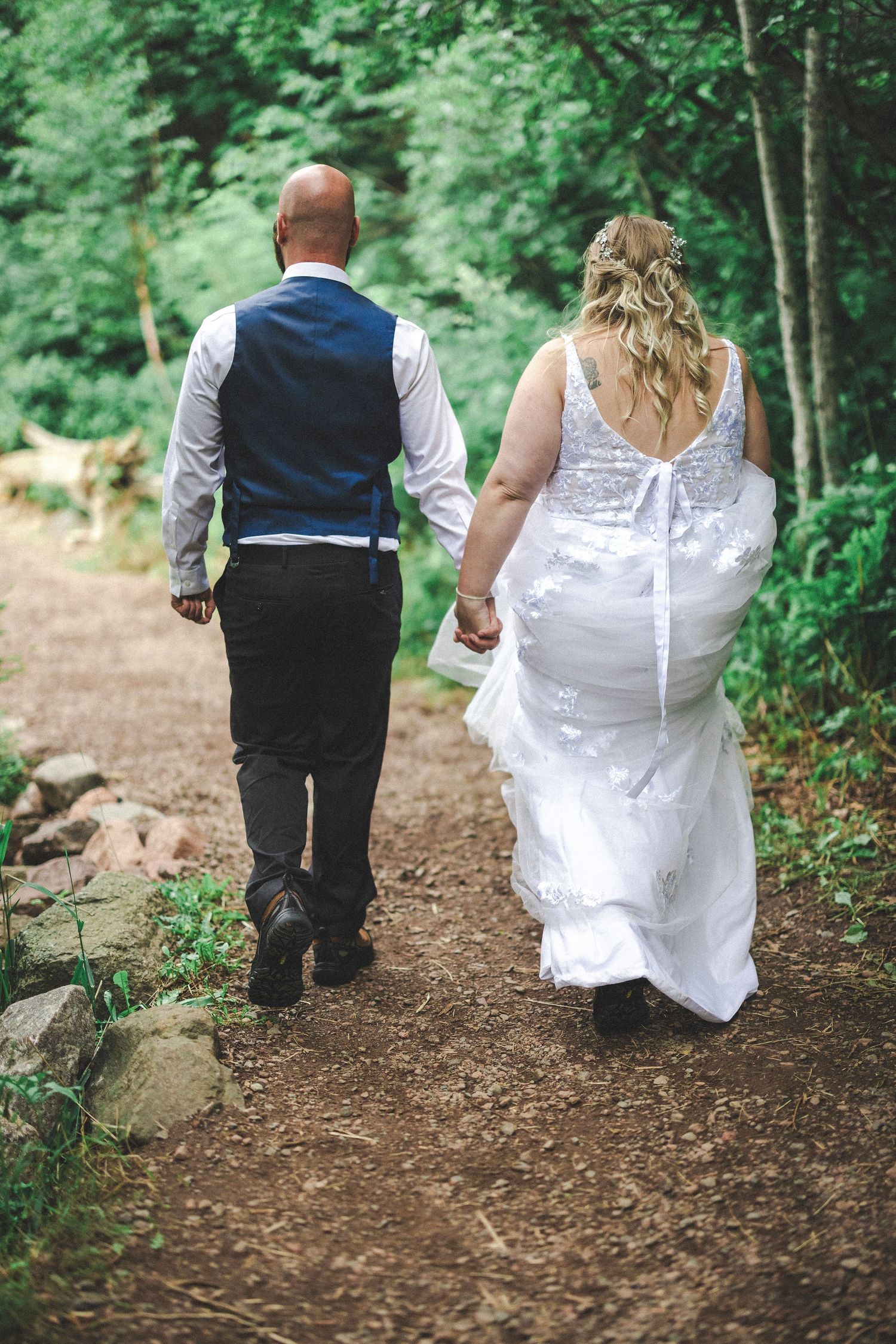 A couple walks down a wooded dirt path on their wedding day.