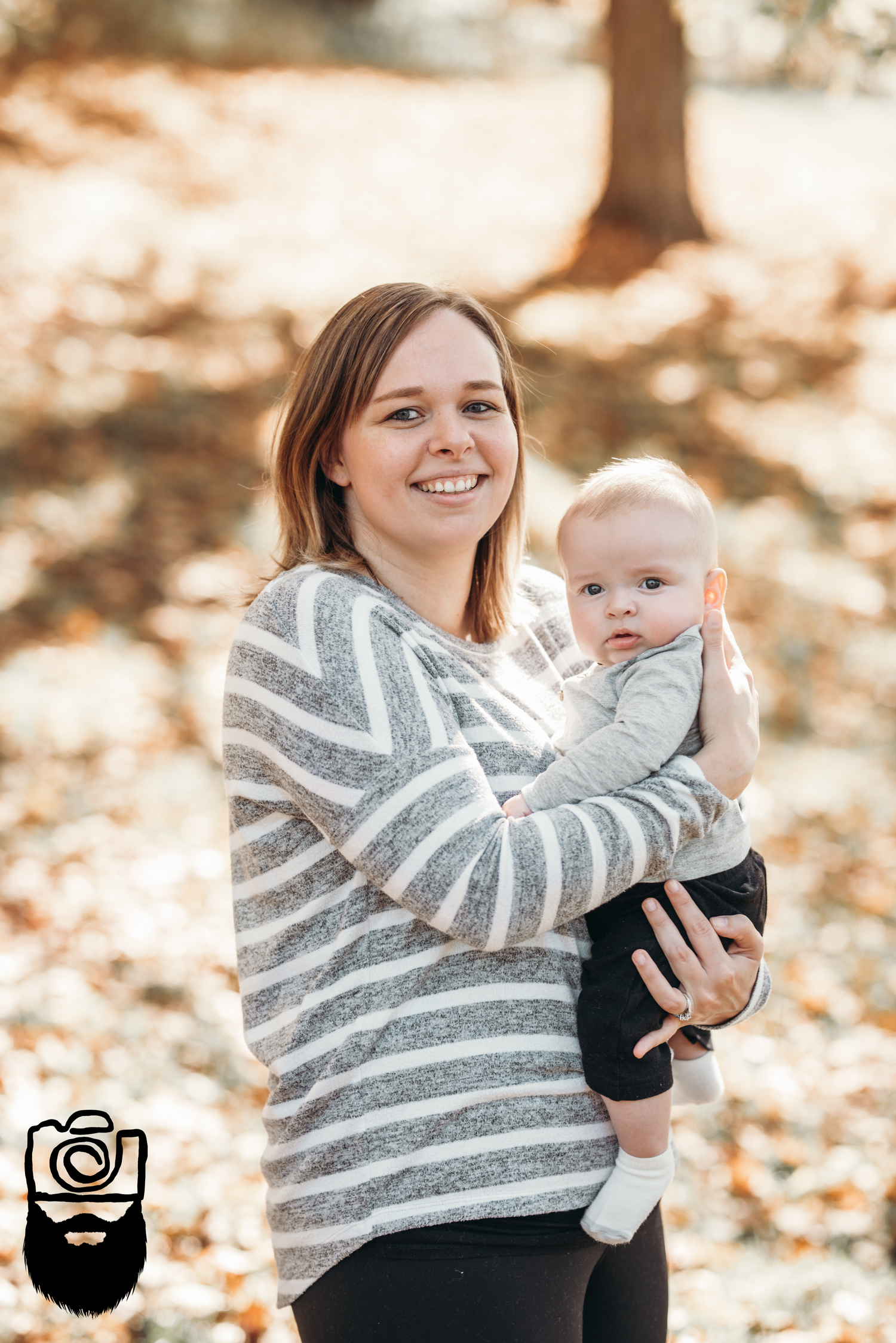 Parent holding baby while wearing striped sweater in autumn setting.