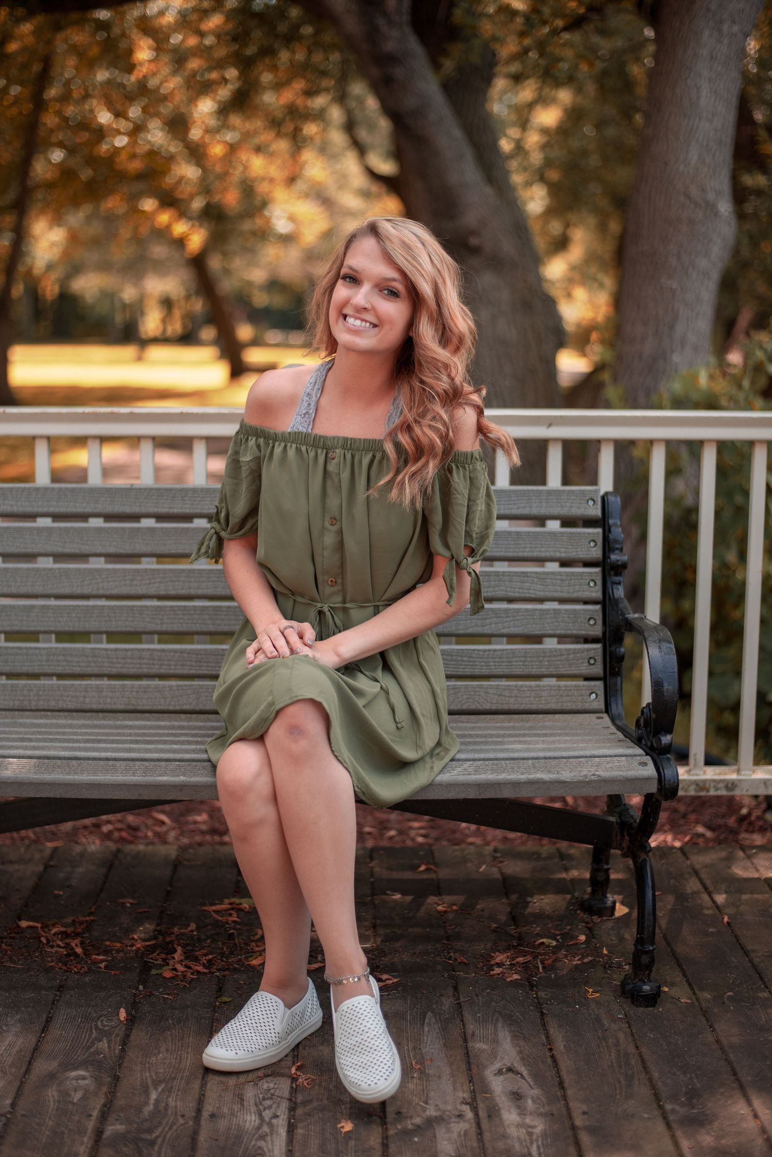 Person in an olive dress sitting on a wooden bench outdoors.