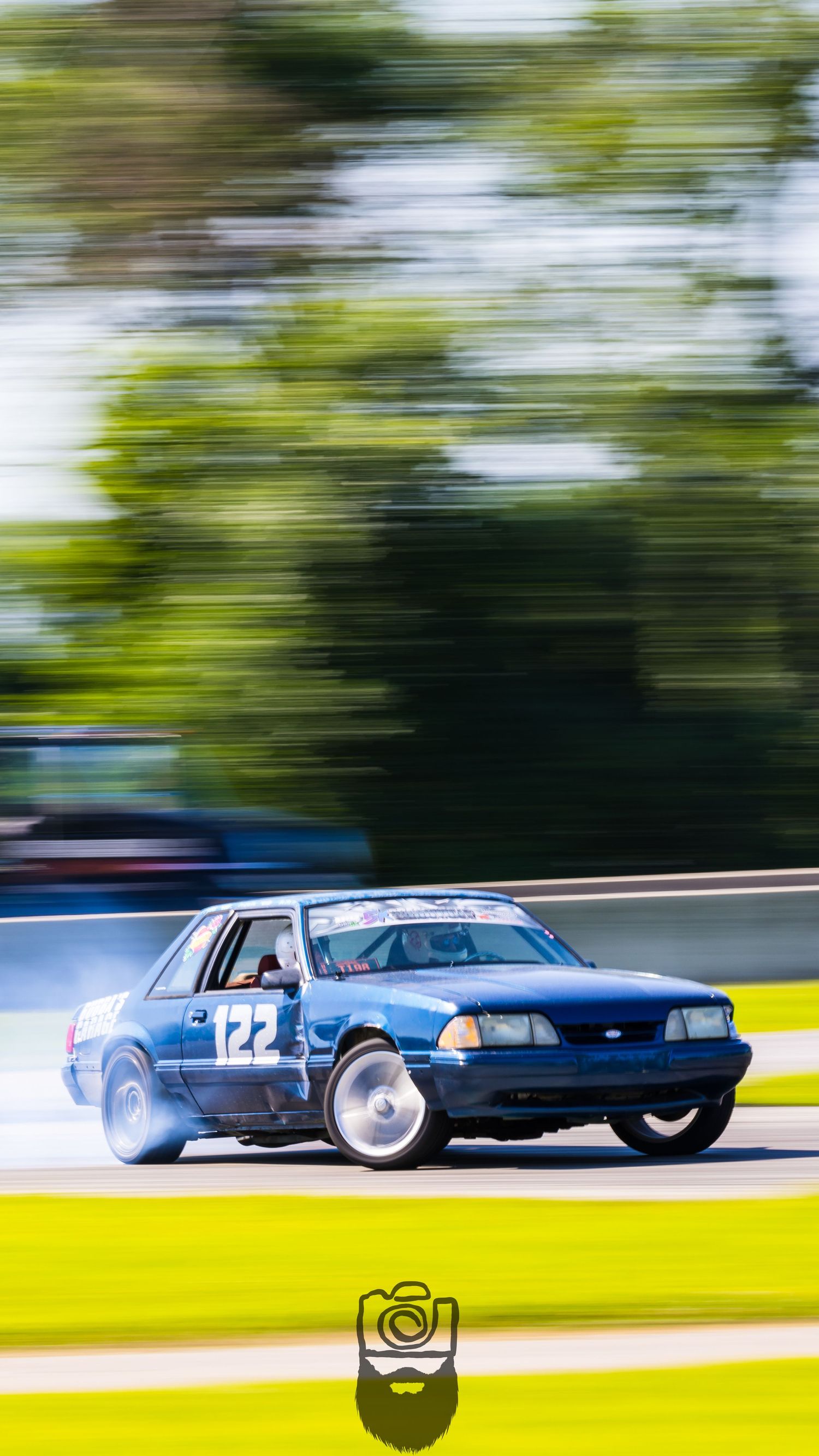 Multiple race cars compete on sunny track with motion blur emphasizing speed.