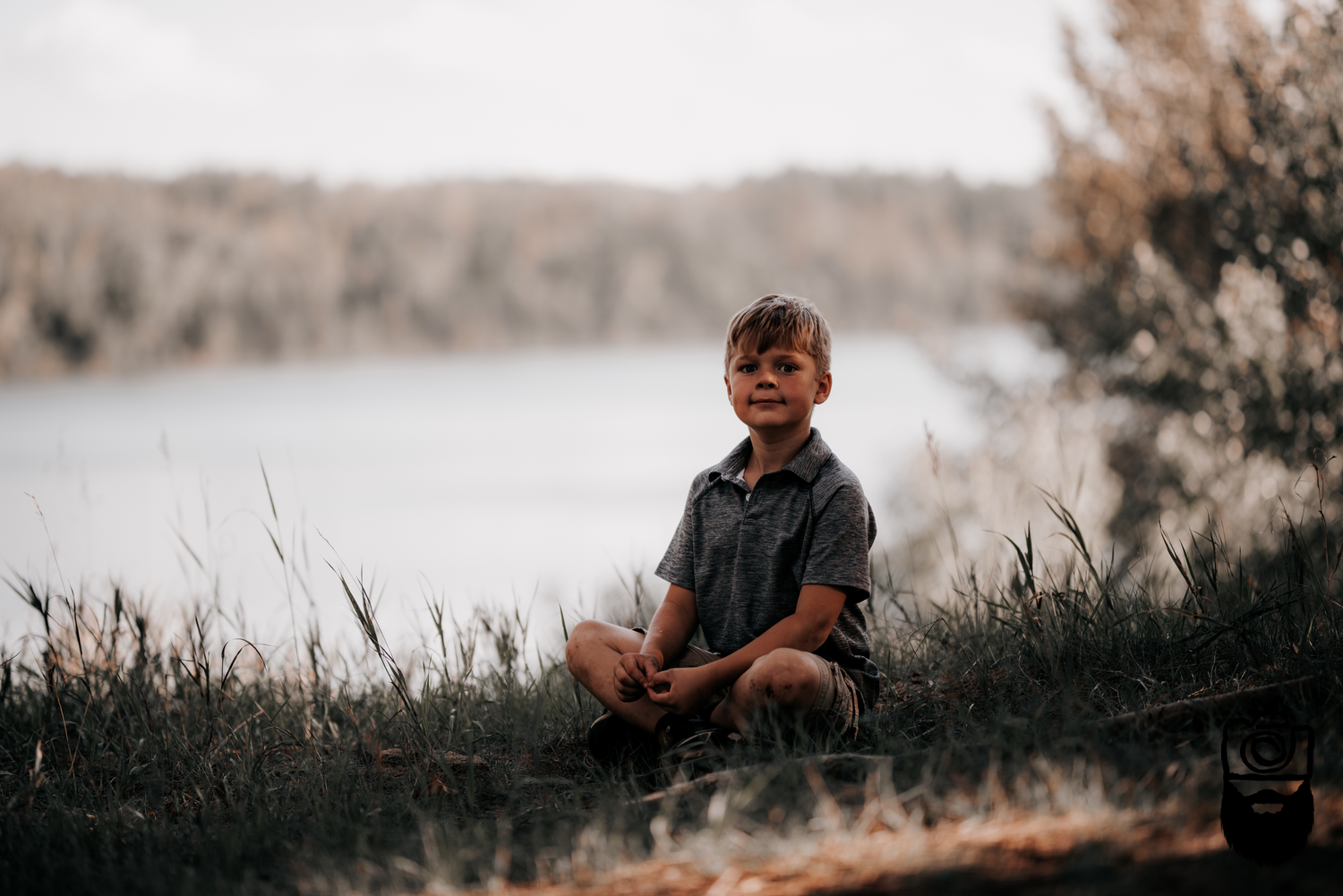 Child sitting on grassy hillside overlooking peaceful lake.