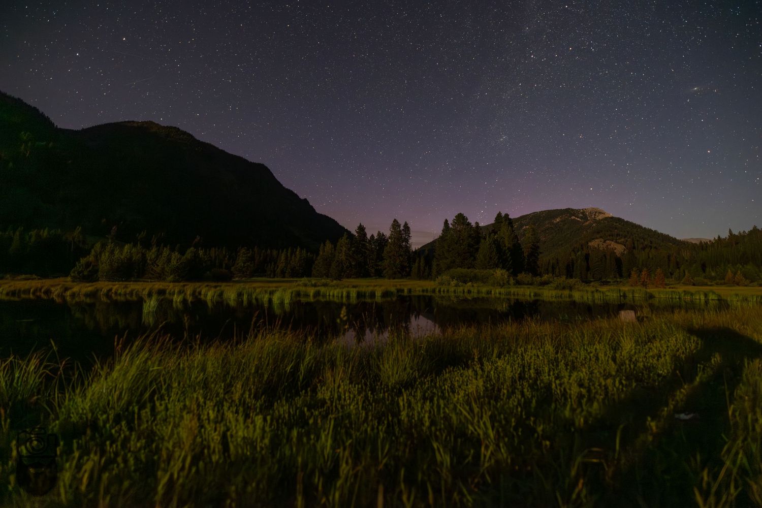 Panoramic nighttime mountain landscape with stars visible in the dark sky.