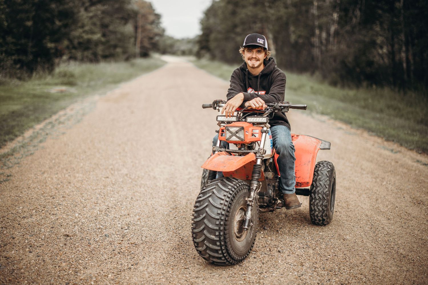 Orange ATV driving on rural dirt road during outdoor photo session.