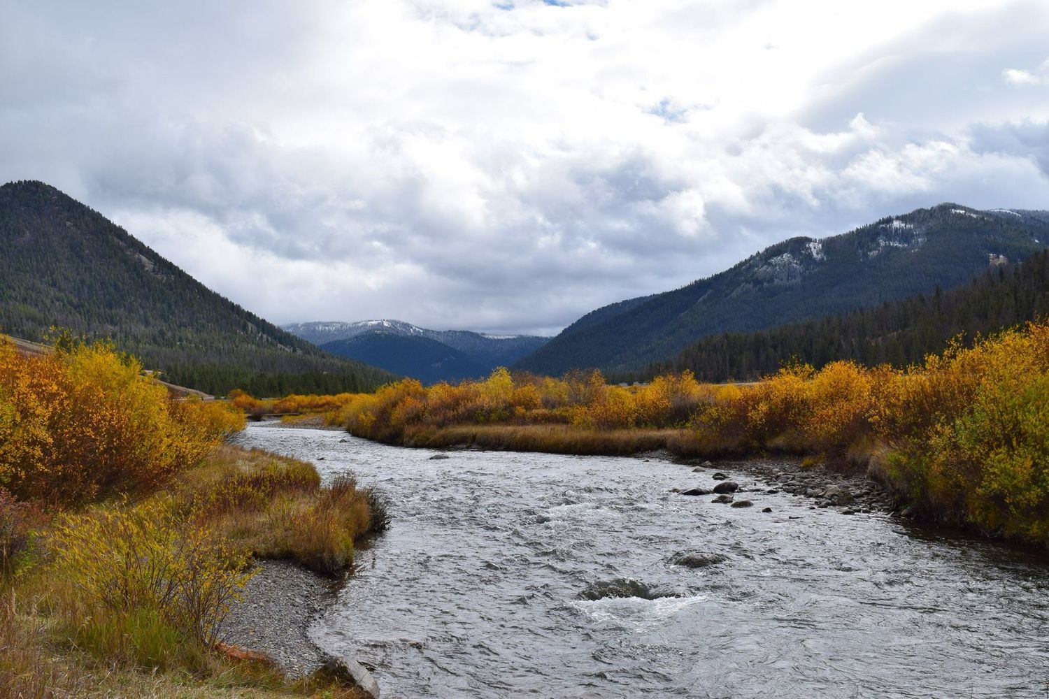 Dramatic mountain vista with golden fall colors along a rushing river.