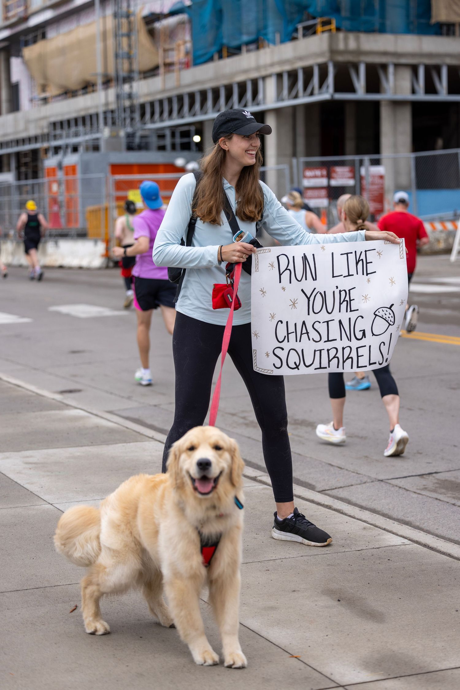 Golden retriever with handler holding humorous sign during race event.