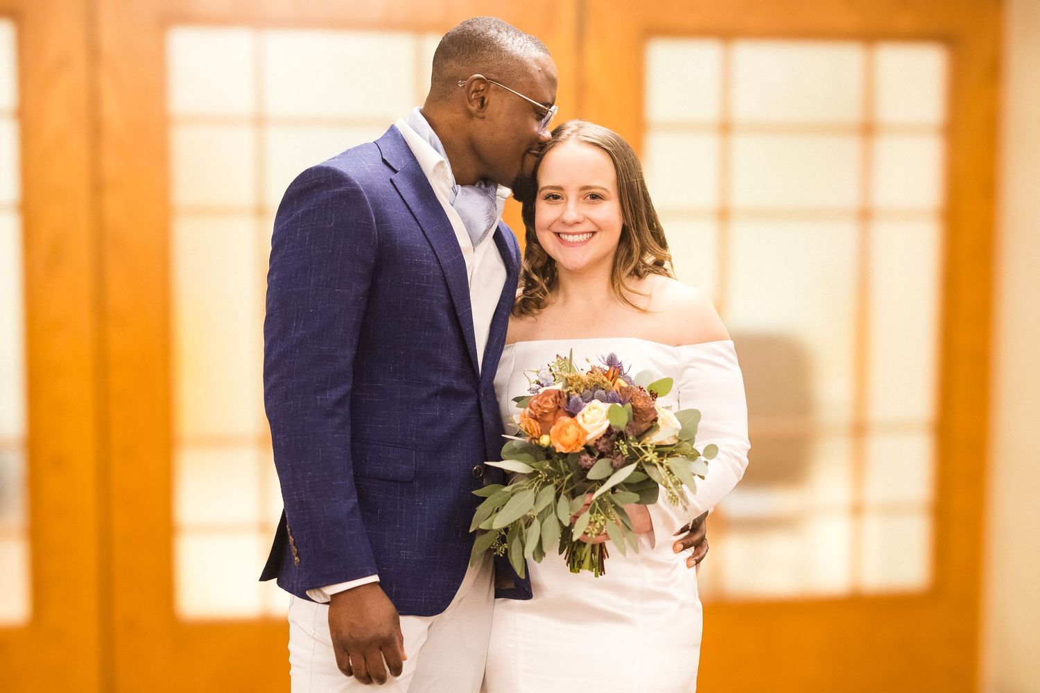 A couple shares a romantic moment in a warmly lit indoor venue with wooden pillars and orange lighting.