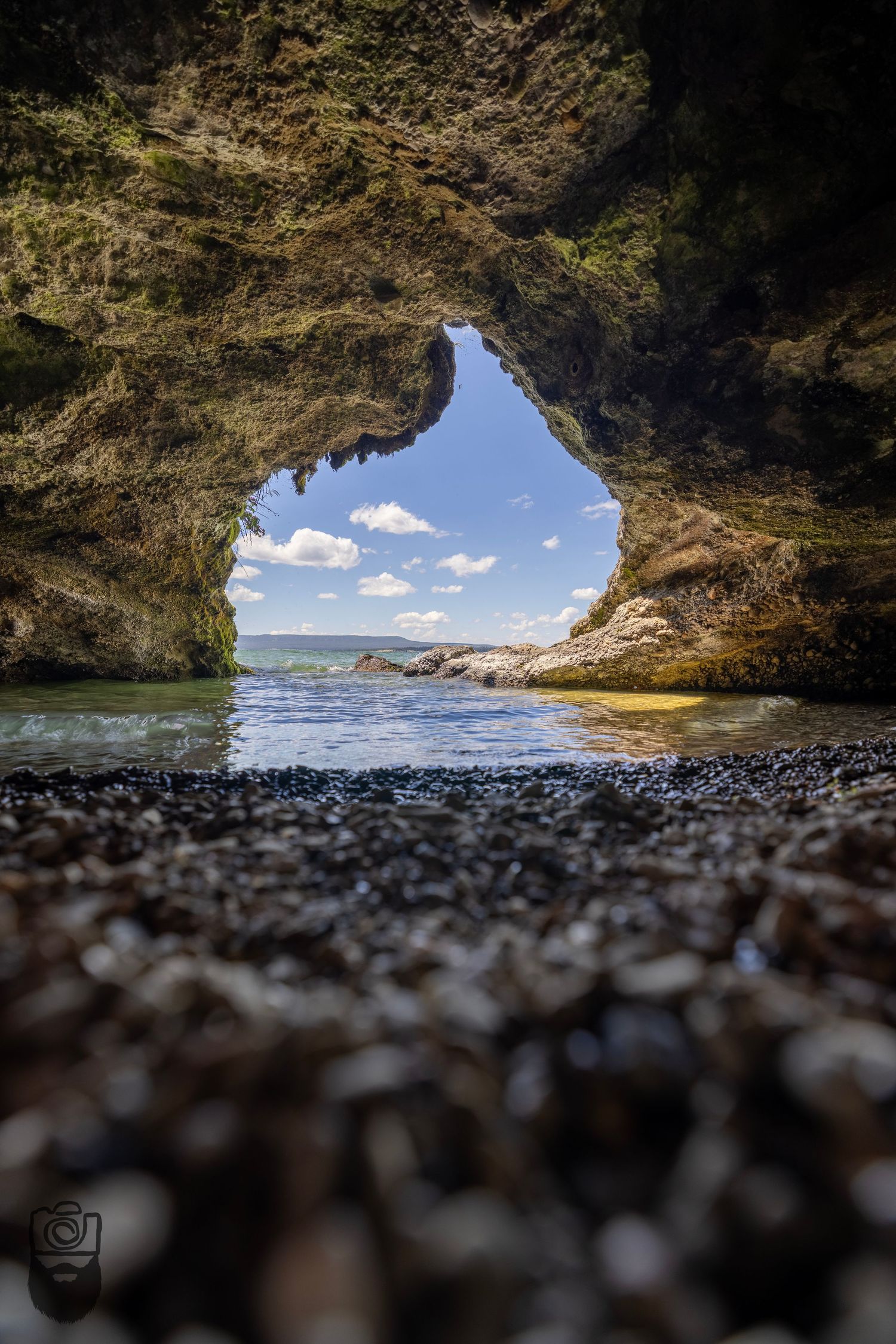View from inside a rocky coastal cave looking out towards the ocean and blue sky.