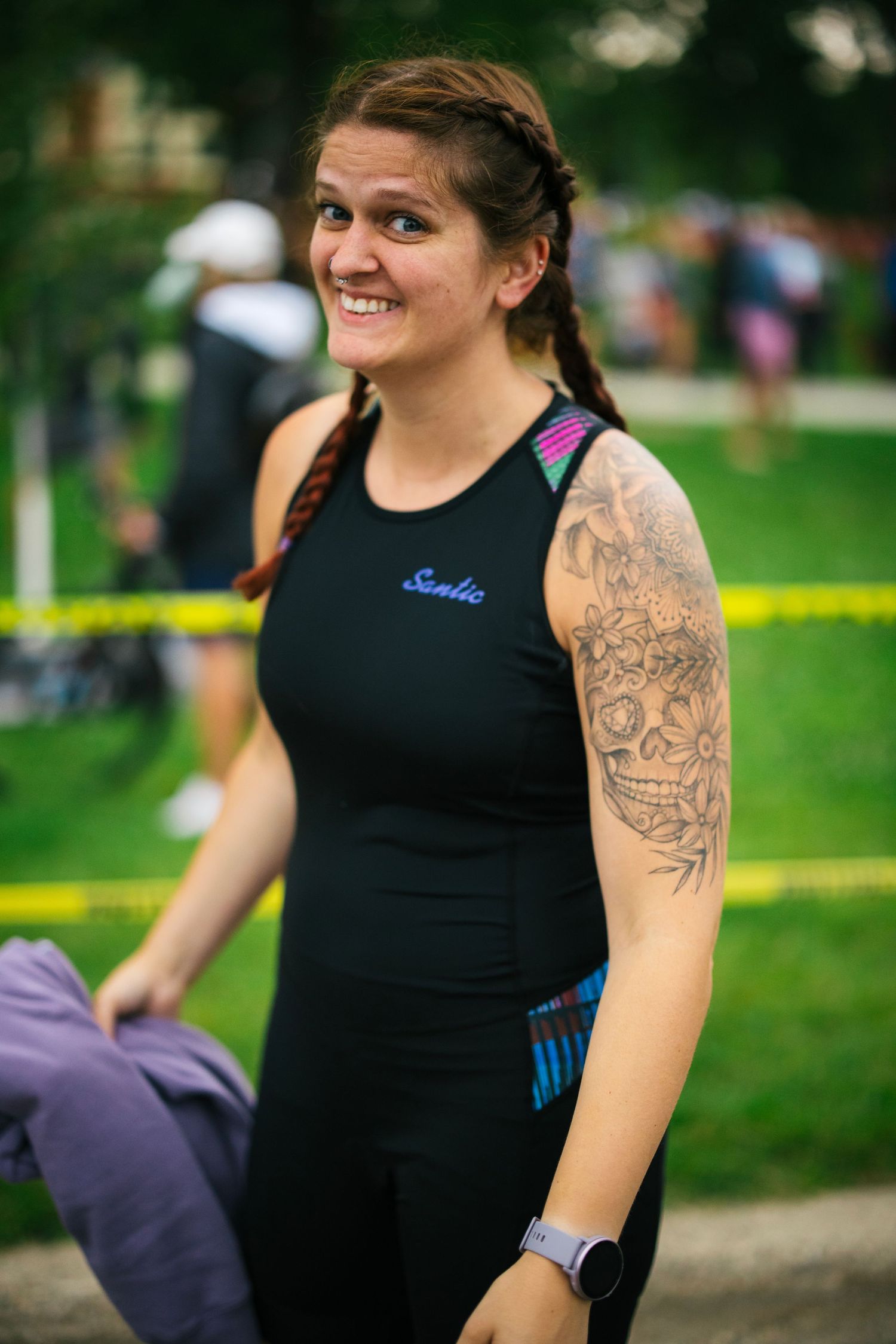 An athlete in black athletic wear with visible tattoos at an outdoor sporting event.