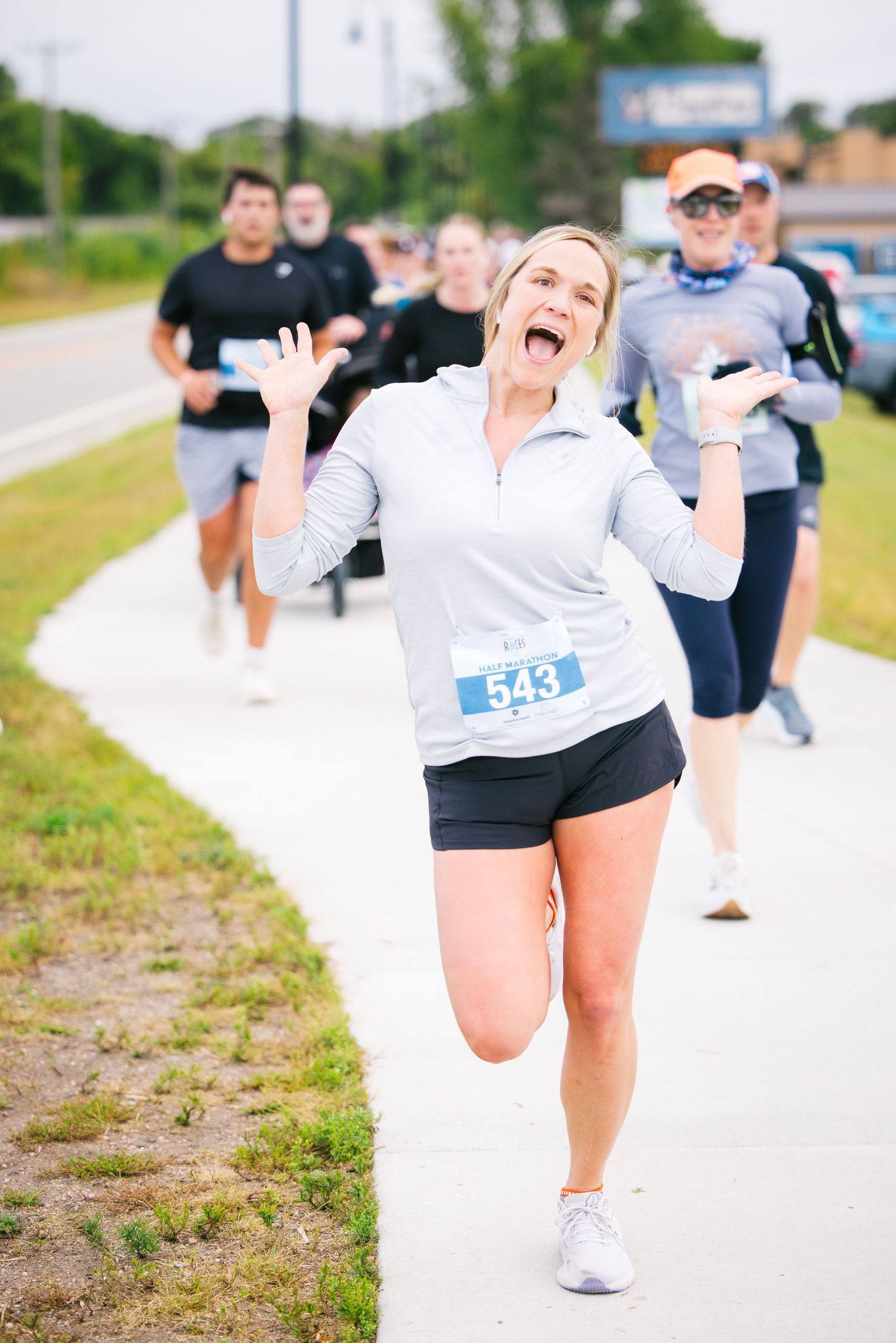 Runner in white top and shorts stretches during an outdoor race event on a sunny day.