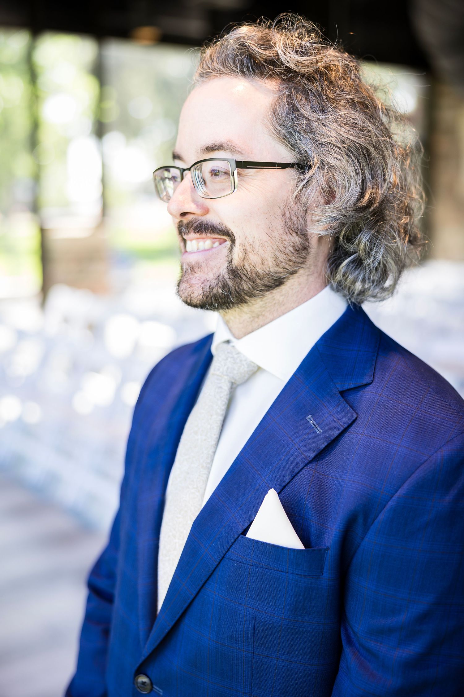Person in navy blue suit and glasses smiling in outdoor portrait series.