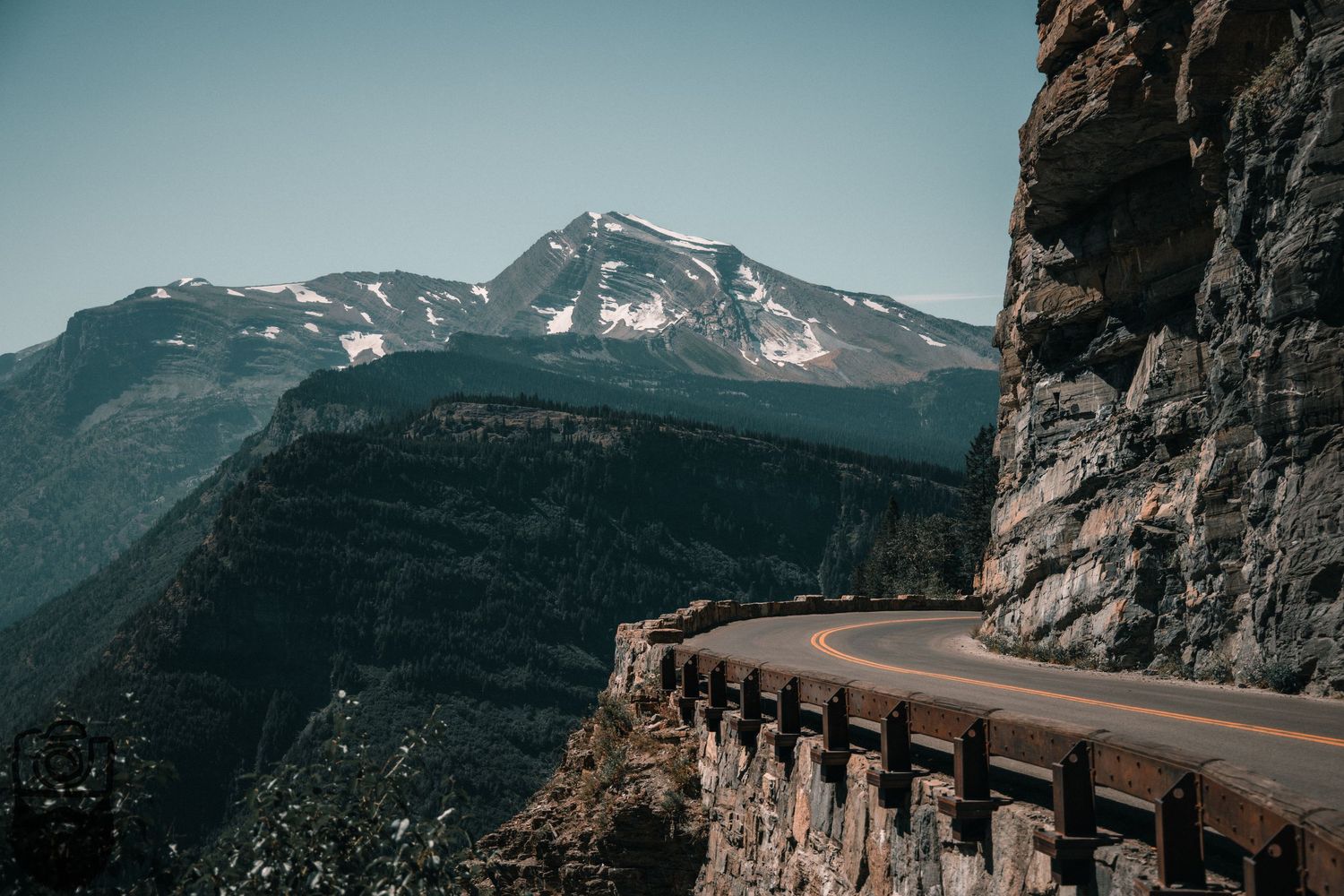 Winding mountain road curves along steep rocky cliffs in dramatic landscape.