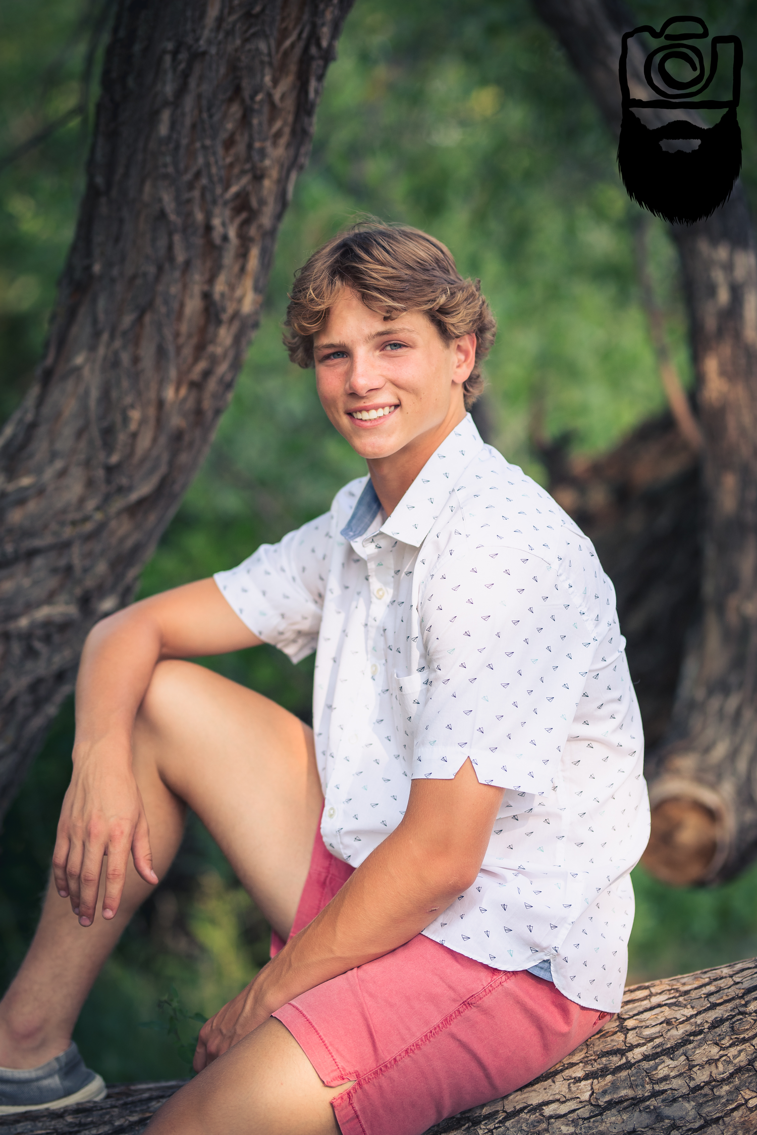 Person in white polka dot shirt and coral shorts sitting casually on tree branch outdoors.