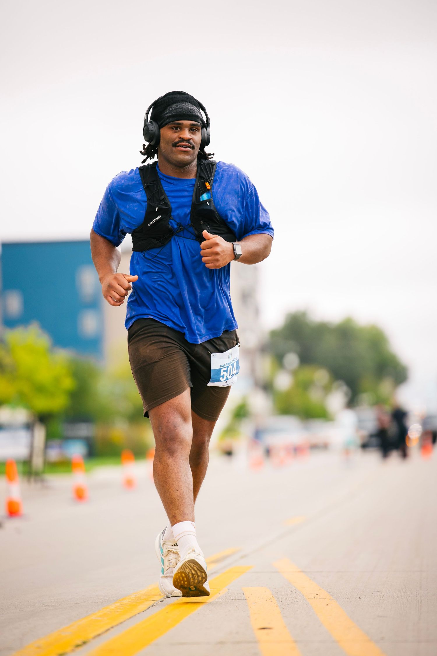 Runner in blue shirt and shorts runs along yellow street lines during race event.
