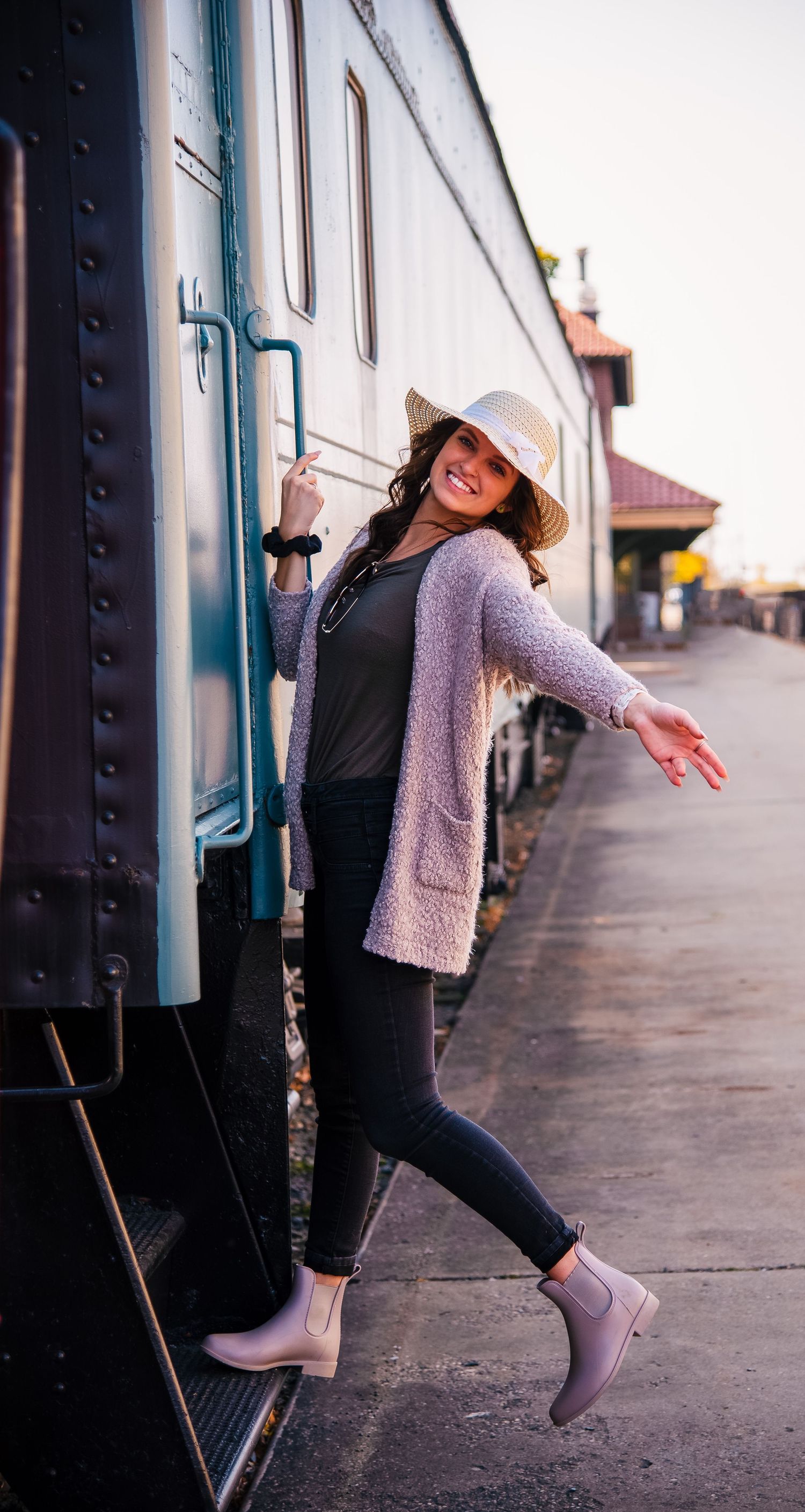 A person in a hat and gray sweater strikes fun poses along a train platform.