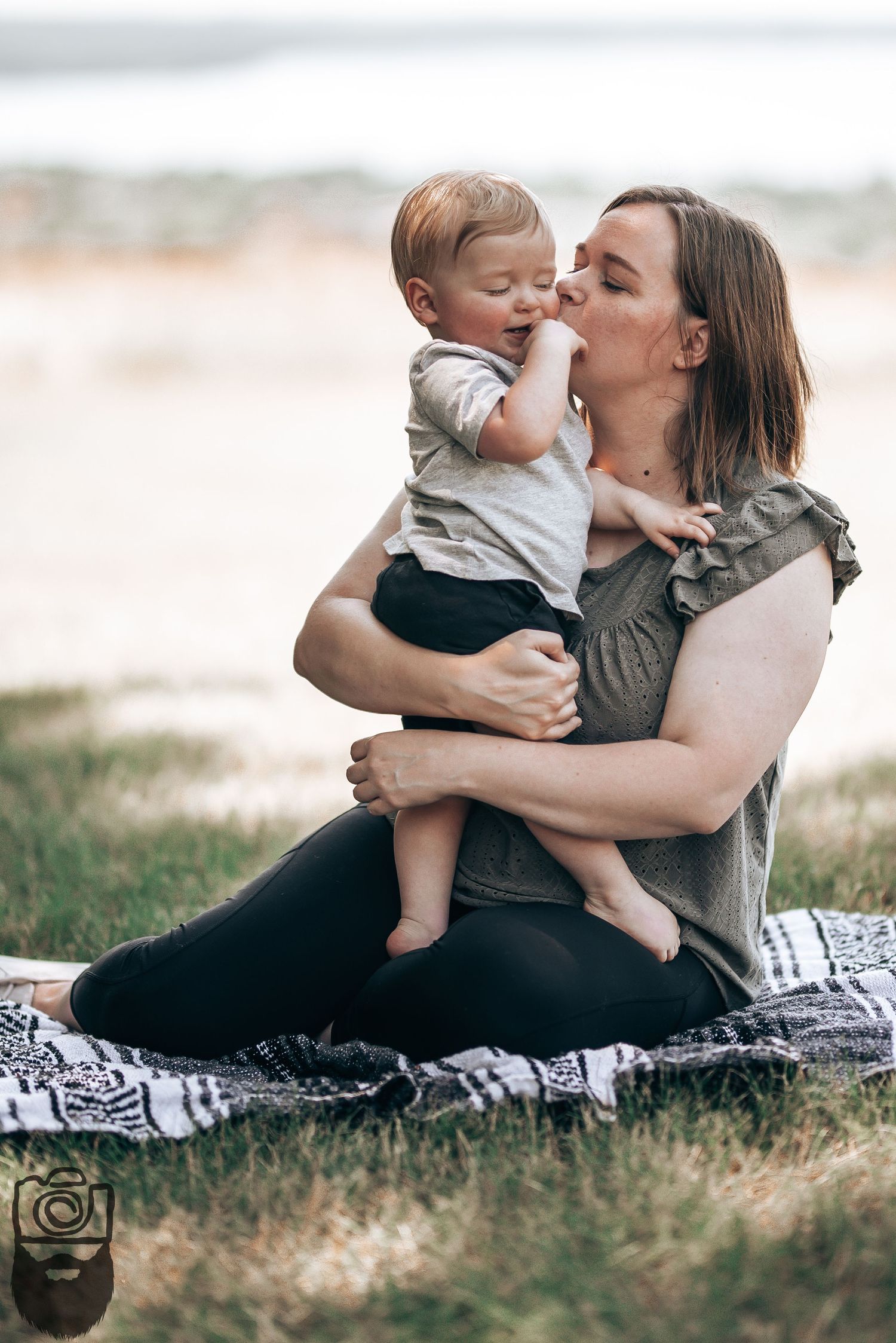 Mother and child sharing affectionate moments while sitting on a blanket outdoors.