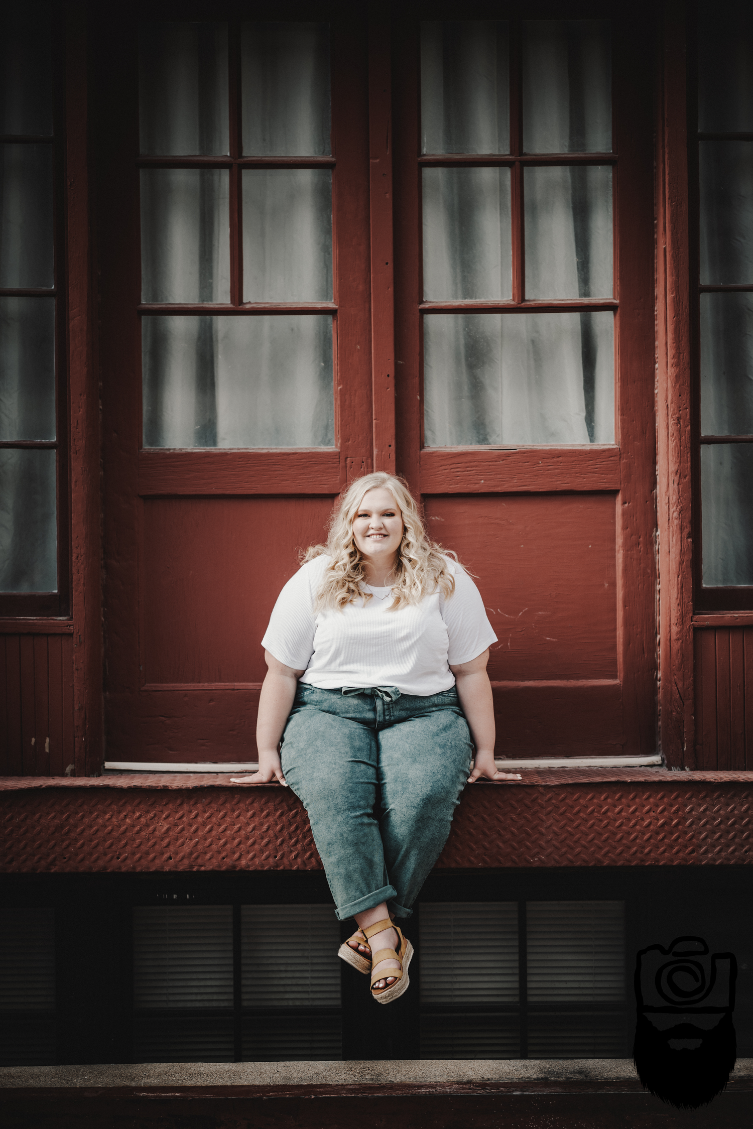 Portrait sitting on red windowsill wearing casual white top and jeans.
