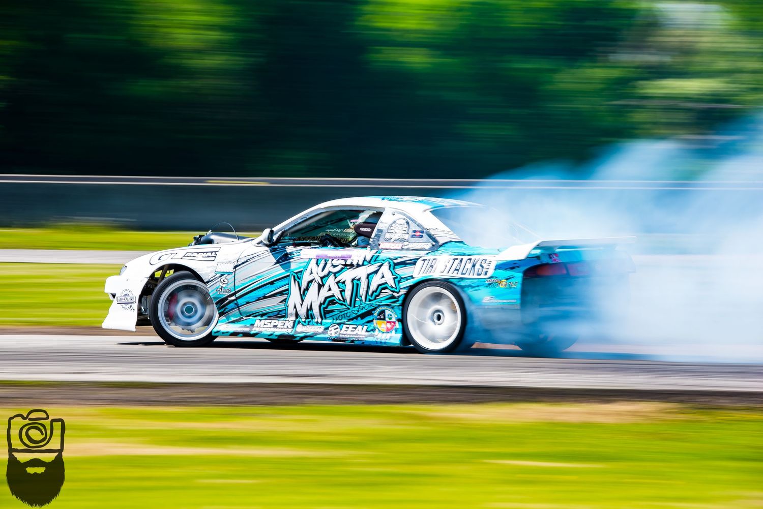 Turquoise drift car performing a high-speed sliding maneuver with tire smoke.