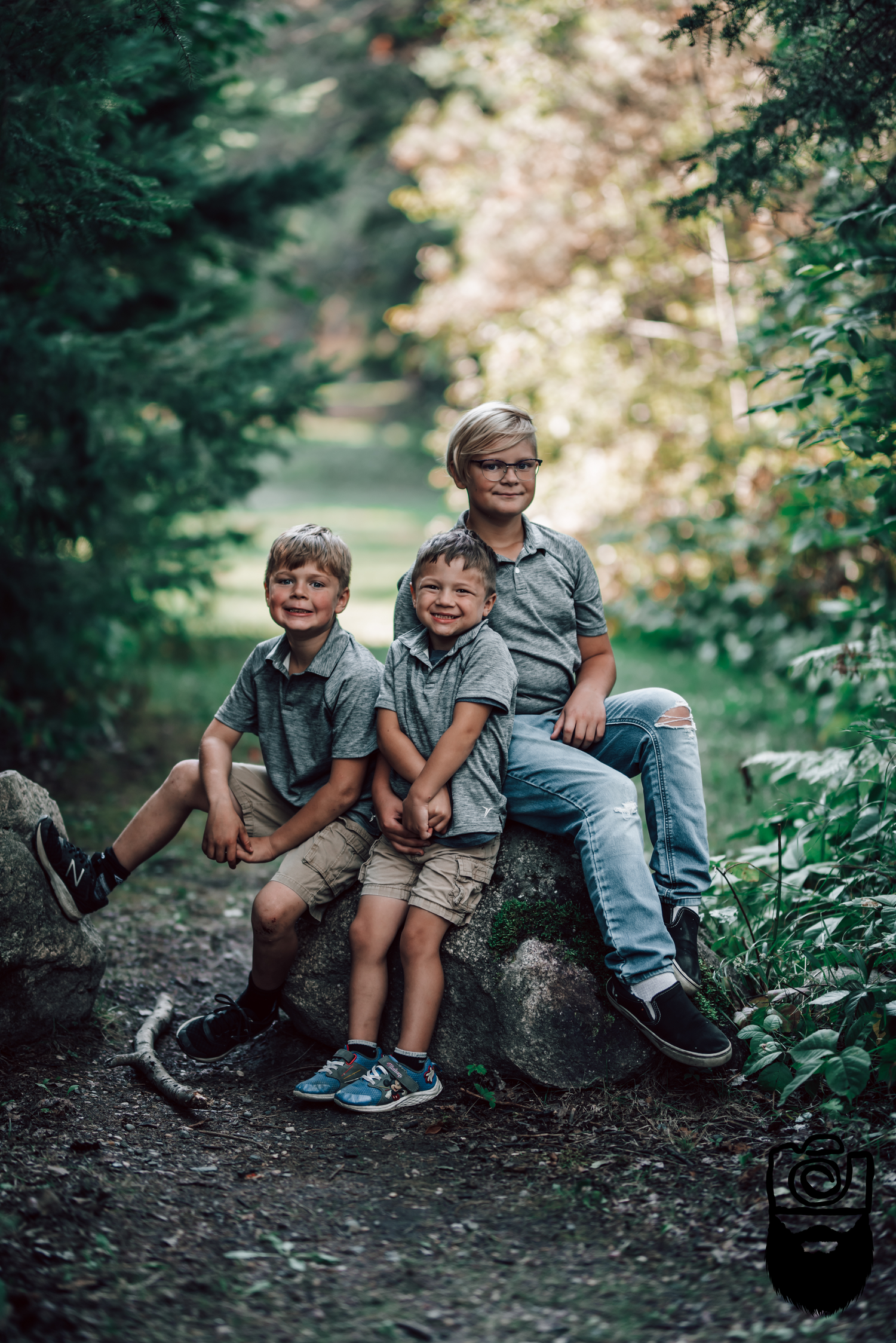 Three people sitting together on a rock in a wooded setting wearing matching gray shirts.