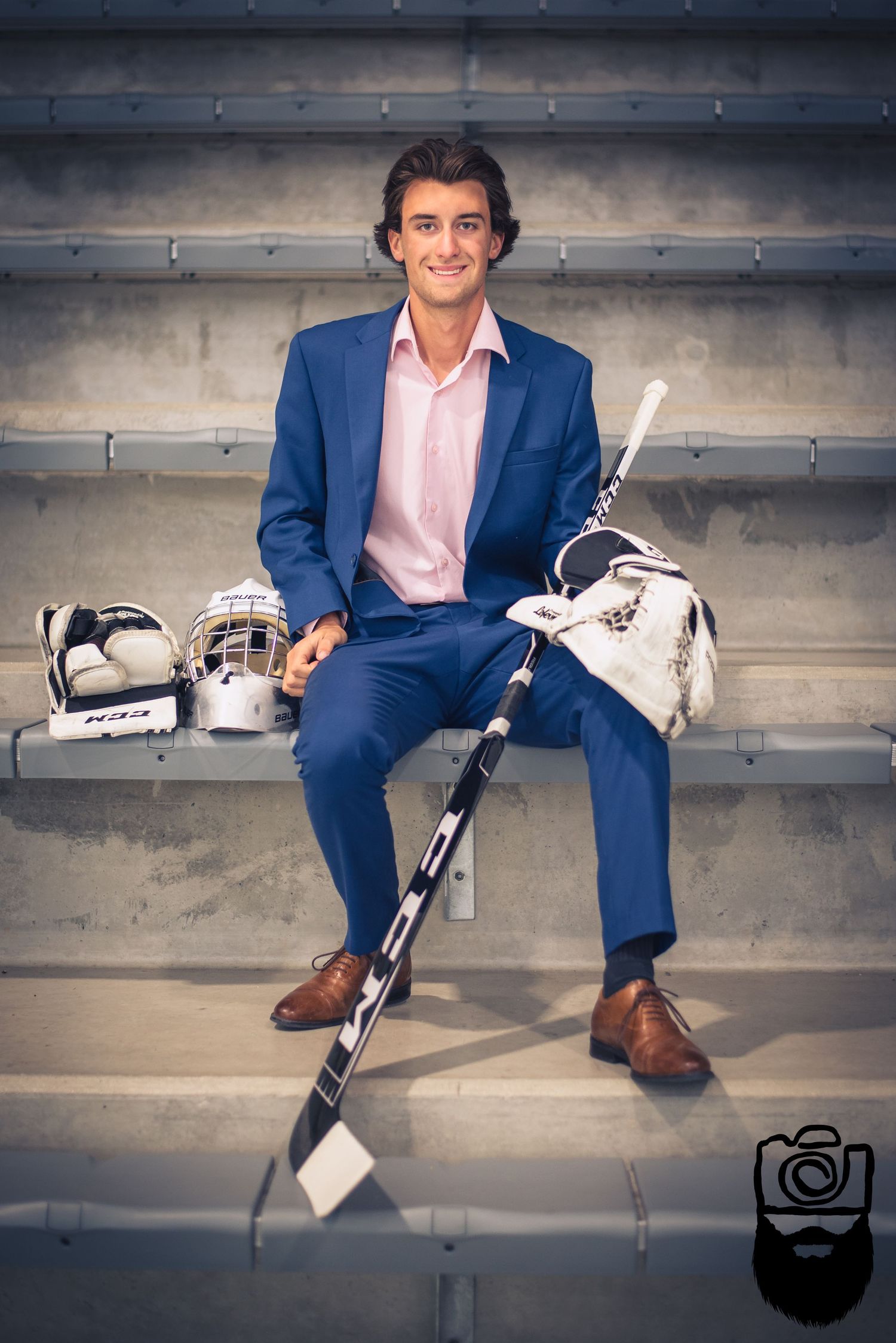 Hockey player in blue suit posing with equipment on concrete stadium seating.