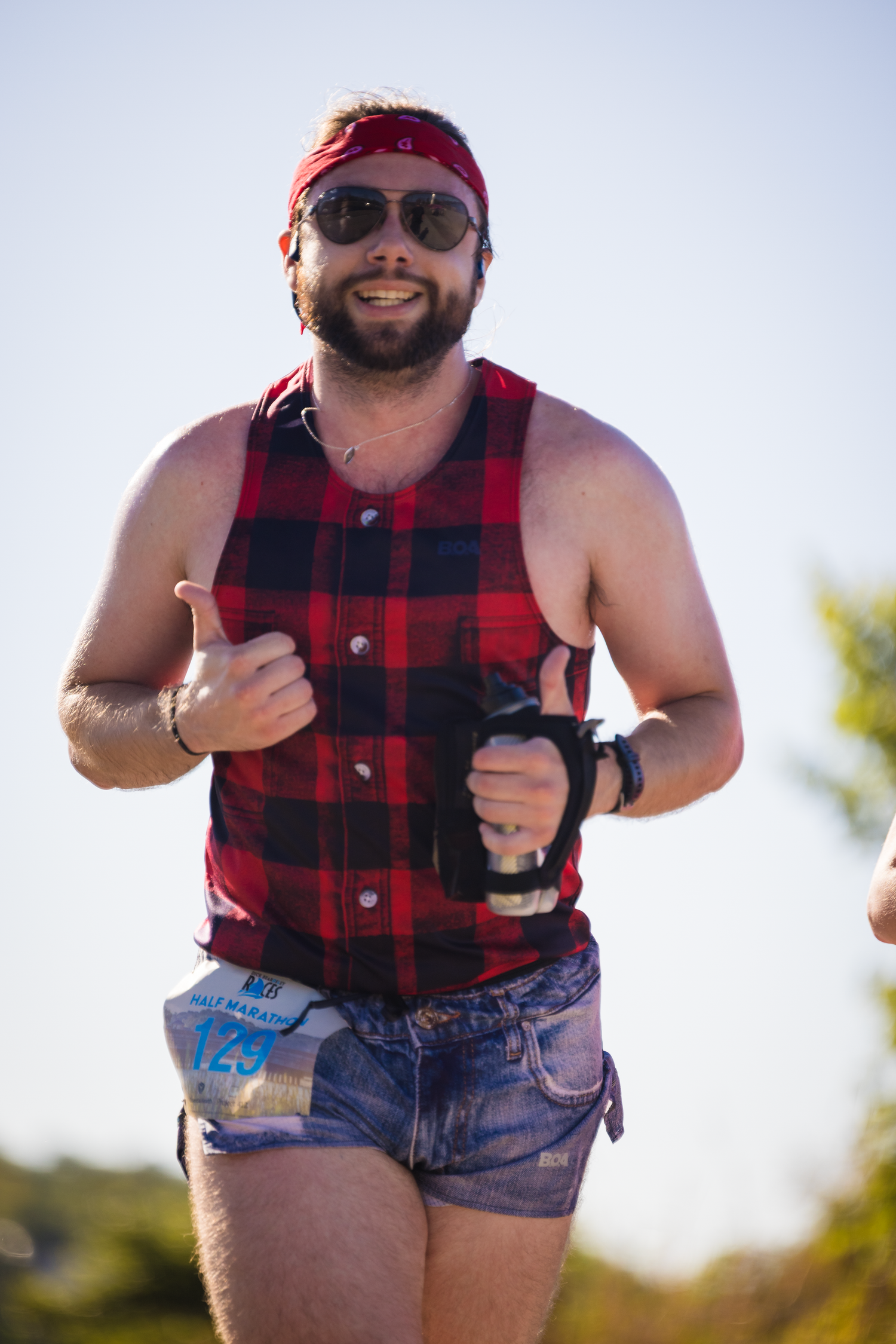 Runner wearing red plaid vest and denim shorts participates enthusiastically in outdoor race event.