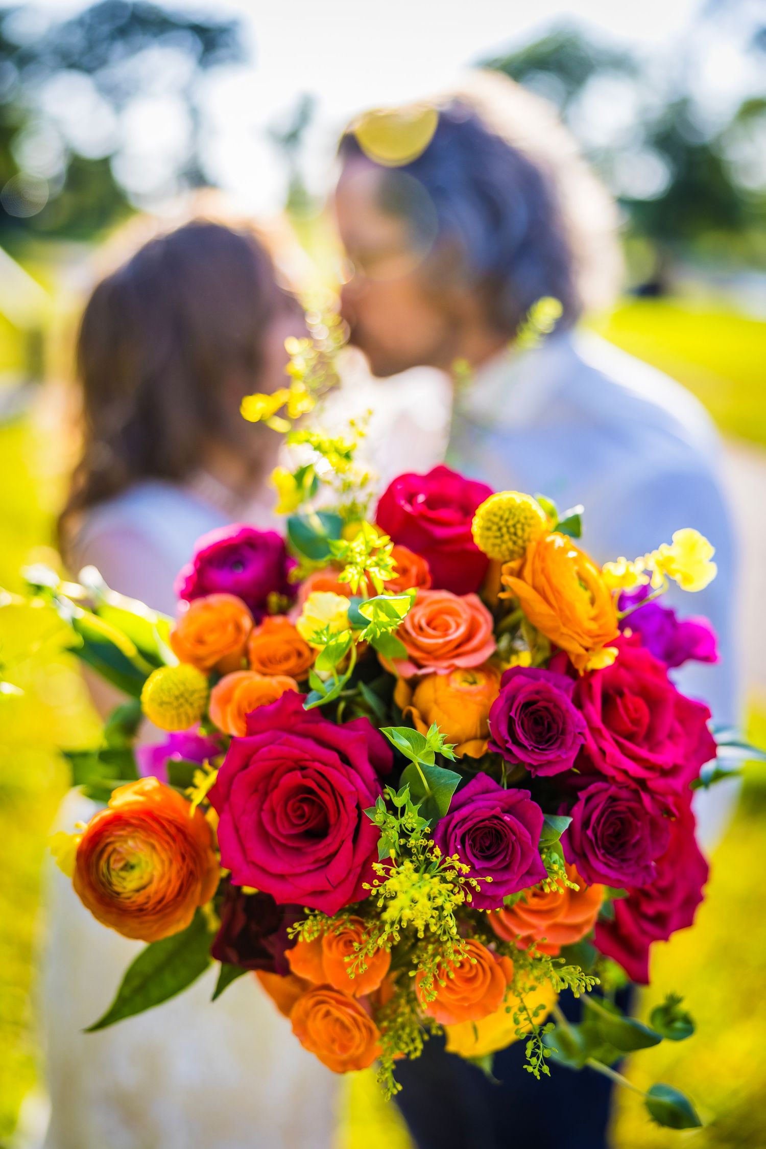 Vibrant wedding bouquet with pink, orange and yellow flowers against blurred background.