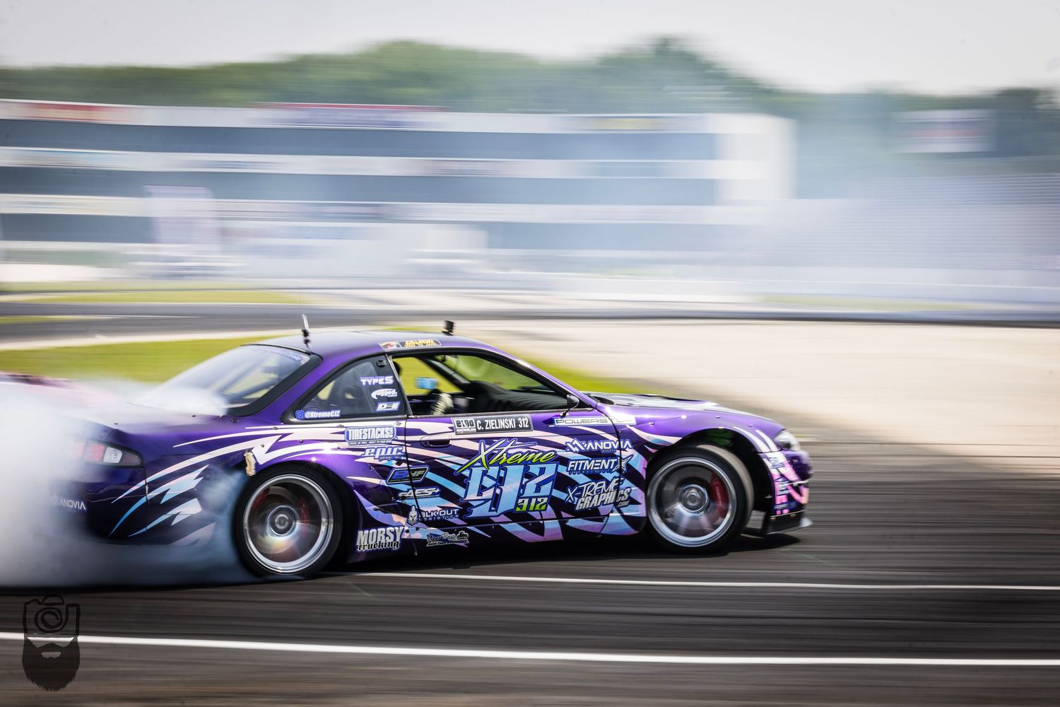 Purple race cars performing synchronized drift maneuvers on racing circuit.