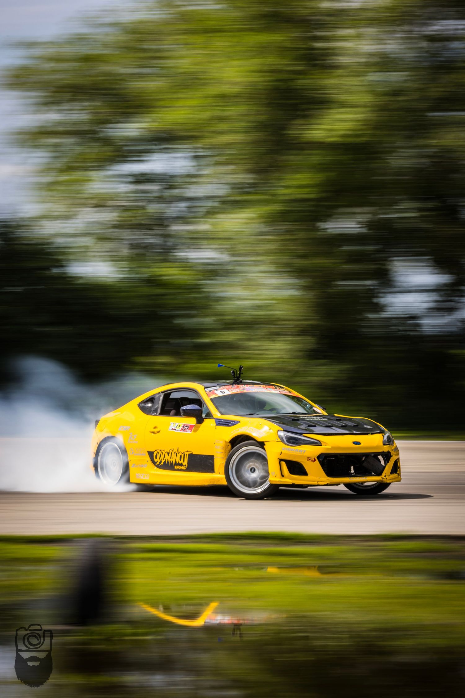 Yellow race car speeding past trees with motion blur effect.