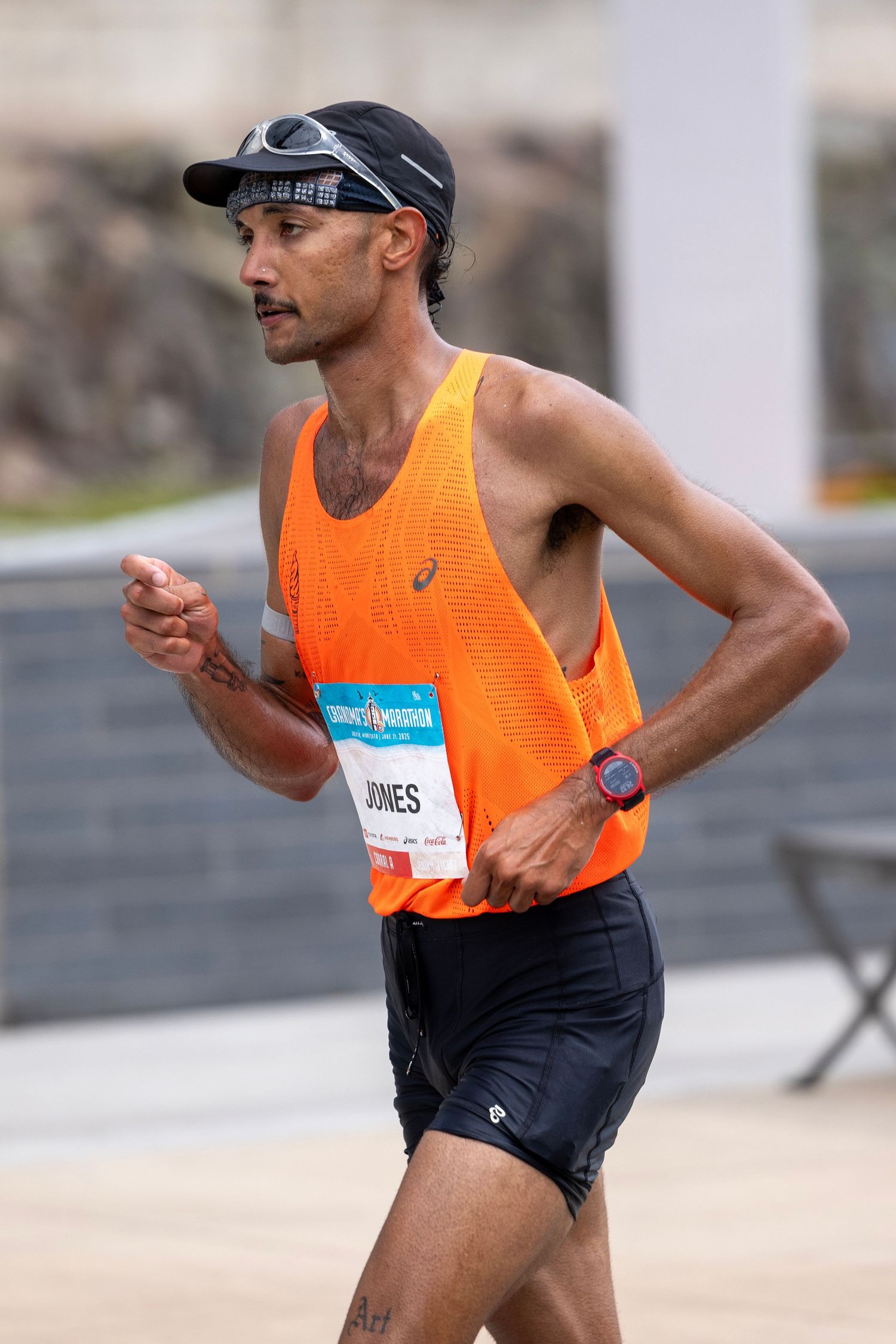 Runner in orange tank top and black shorts checks smartwatch while running on urban street.