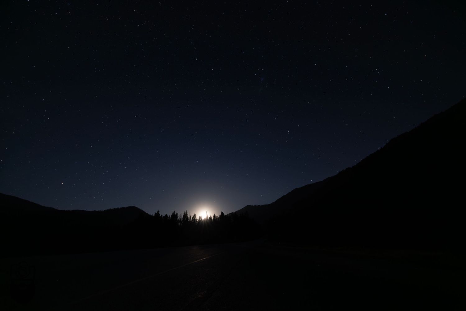 Dark mountain silhouettes against a night sky with moonlight peeking over the ridge.