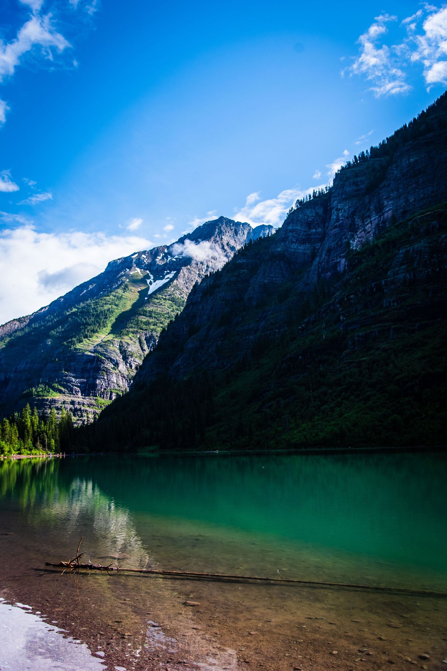 Crystal clear alpine lake reflecting majestic mountain peaks under bright blue skies.