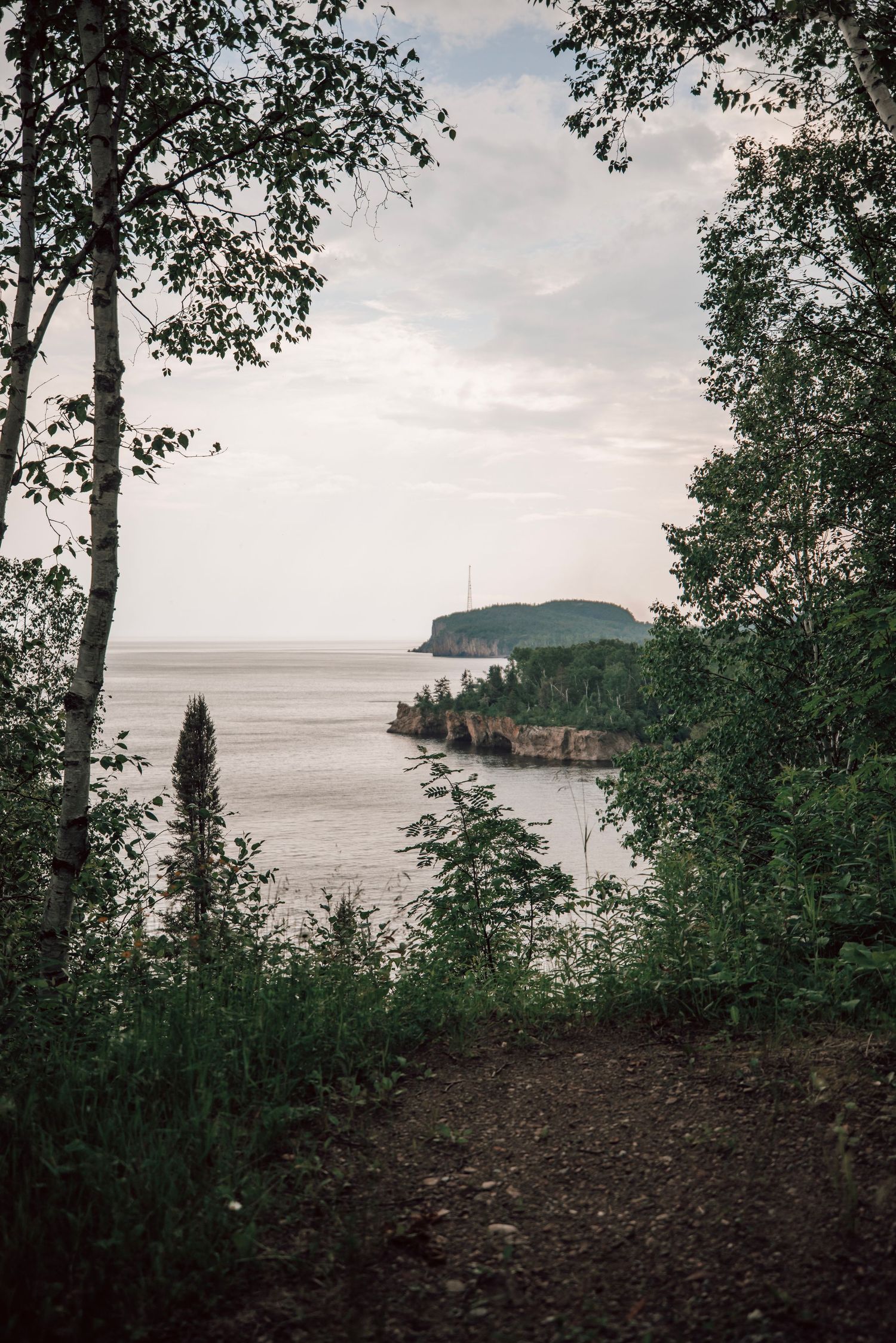 Elevated view of a coastal bay with forested cliffs and calm waters under cloudy skies.