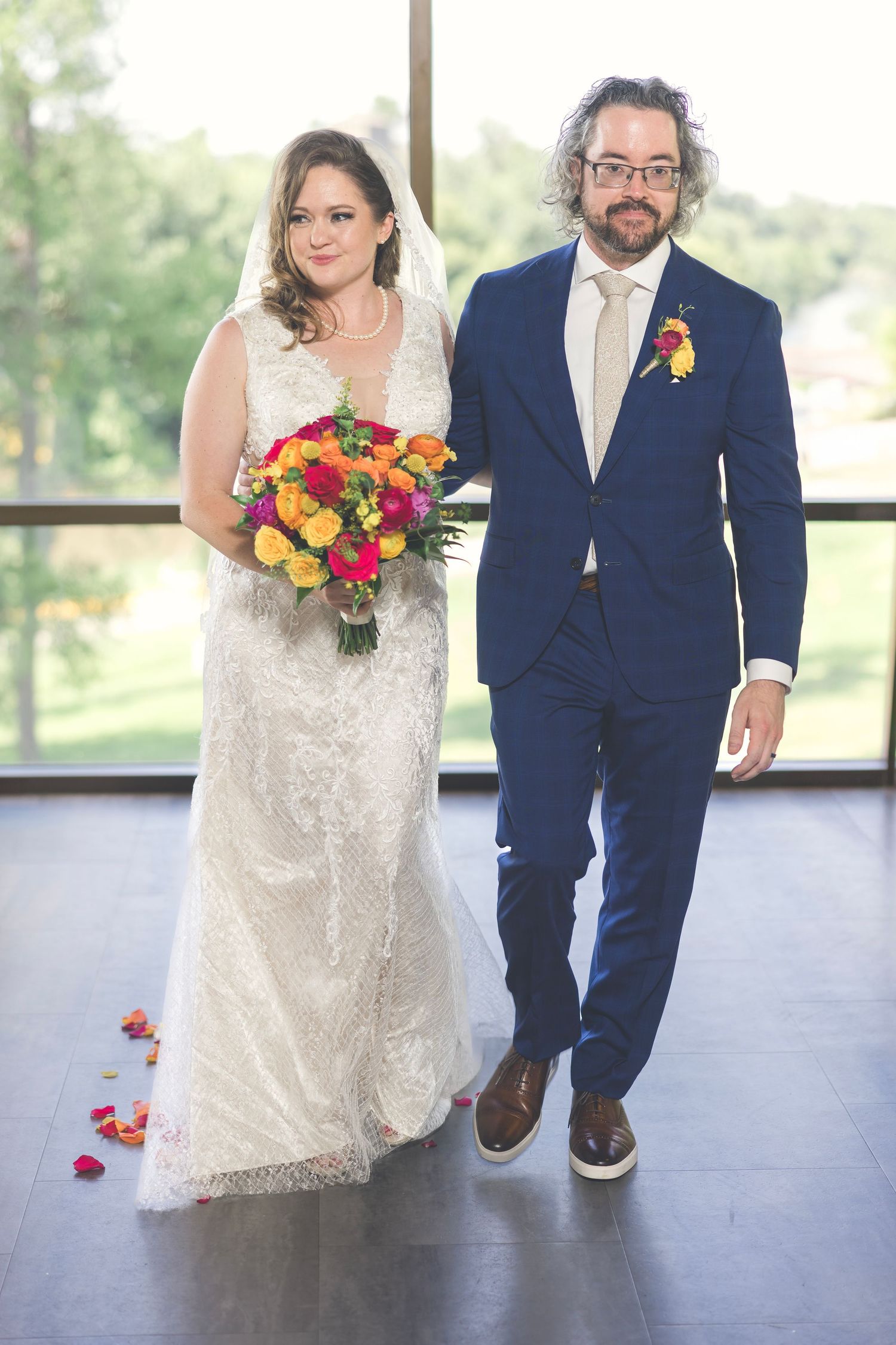 Wedding couple walking together, bride holding colorful bouquet against navy suit.