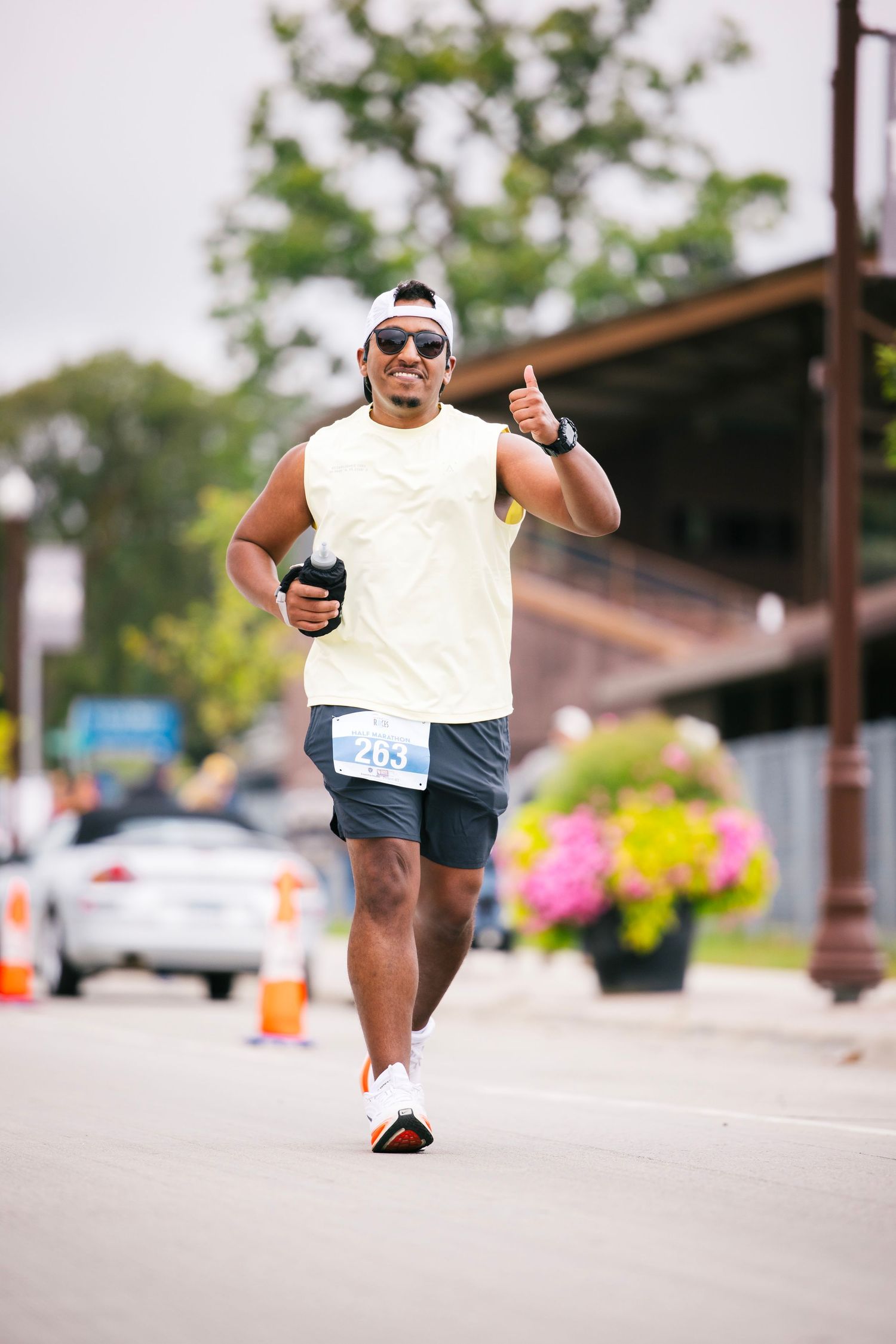 Runner in white t-shirt and shorts strikes dynamic pose during outdoor race on sunny street.