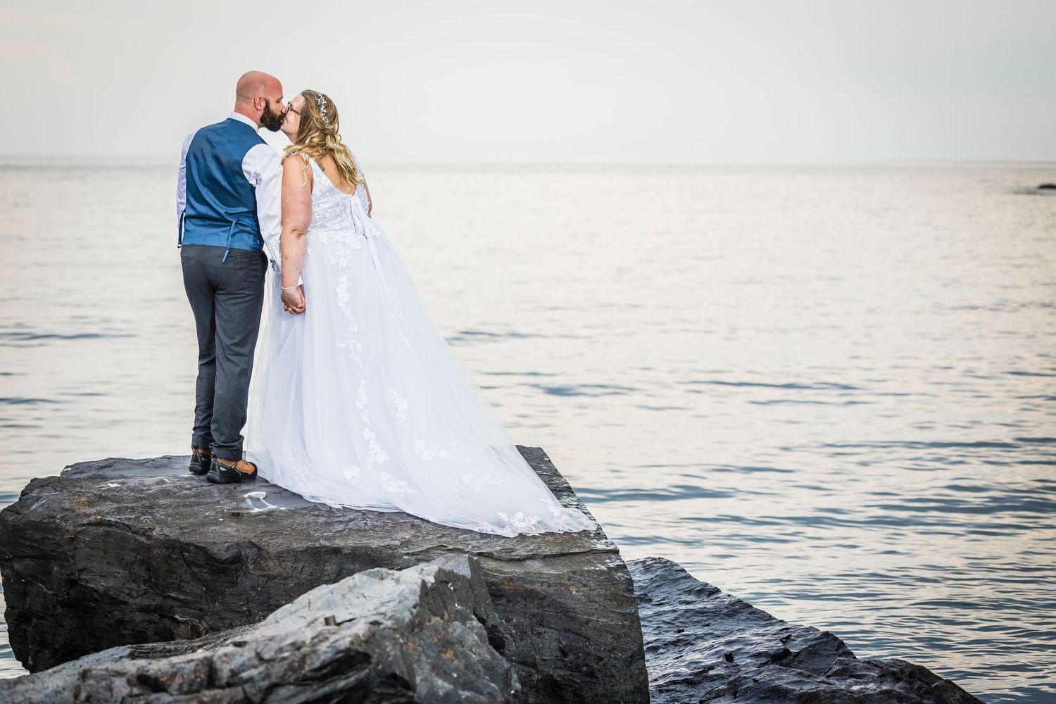 A couple poses on rocky coastal cliffs during their wedding photoshoot at sunset.