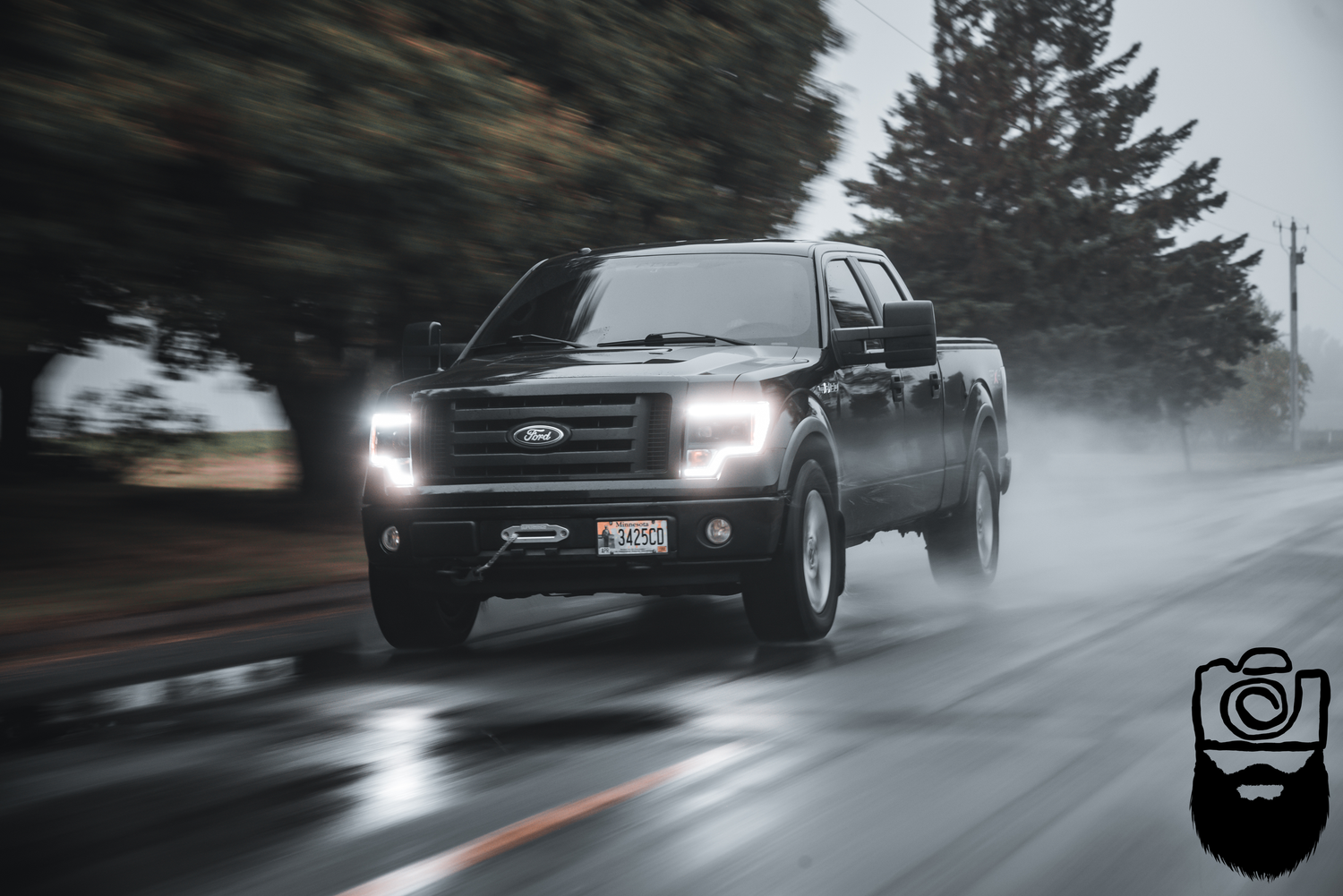 Black sports cars driving in wet conditions on a dark, rainy road.